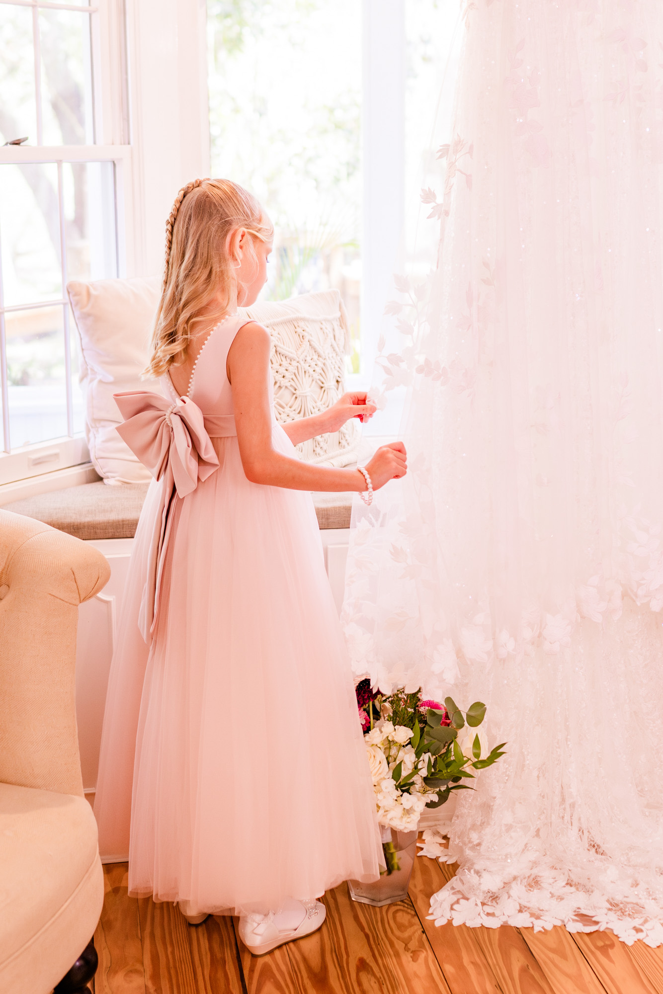 Young flower girl admiring the bride’s wedding dress in a bright getting-ready room.