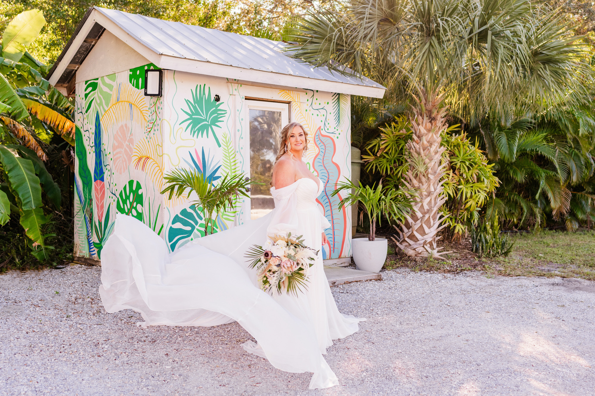 Bride in a flowing white wedding dress in front of the colorful tropical mural at The Treehouse Vero Beach.