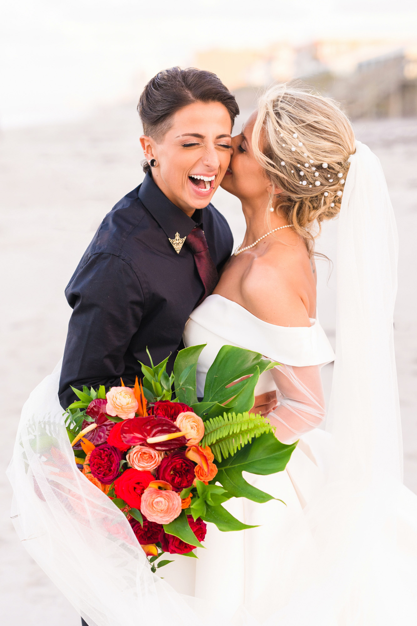 Bride kissing her partner’s cheek while holding a bright tropical bouquet.