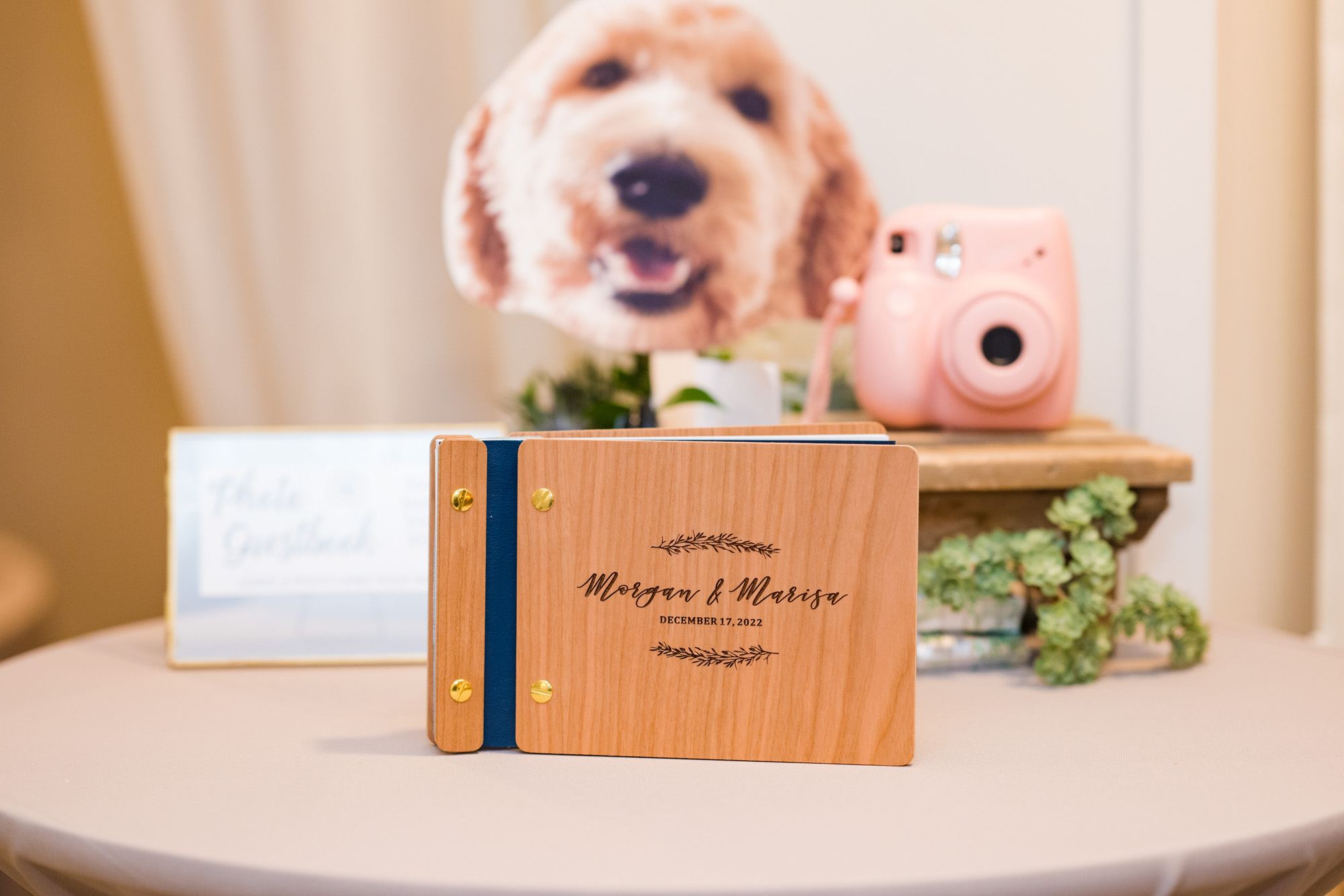 Personalized wooden wedding guest book for Morgan and Marisa displayed beside a pink instant camera.