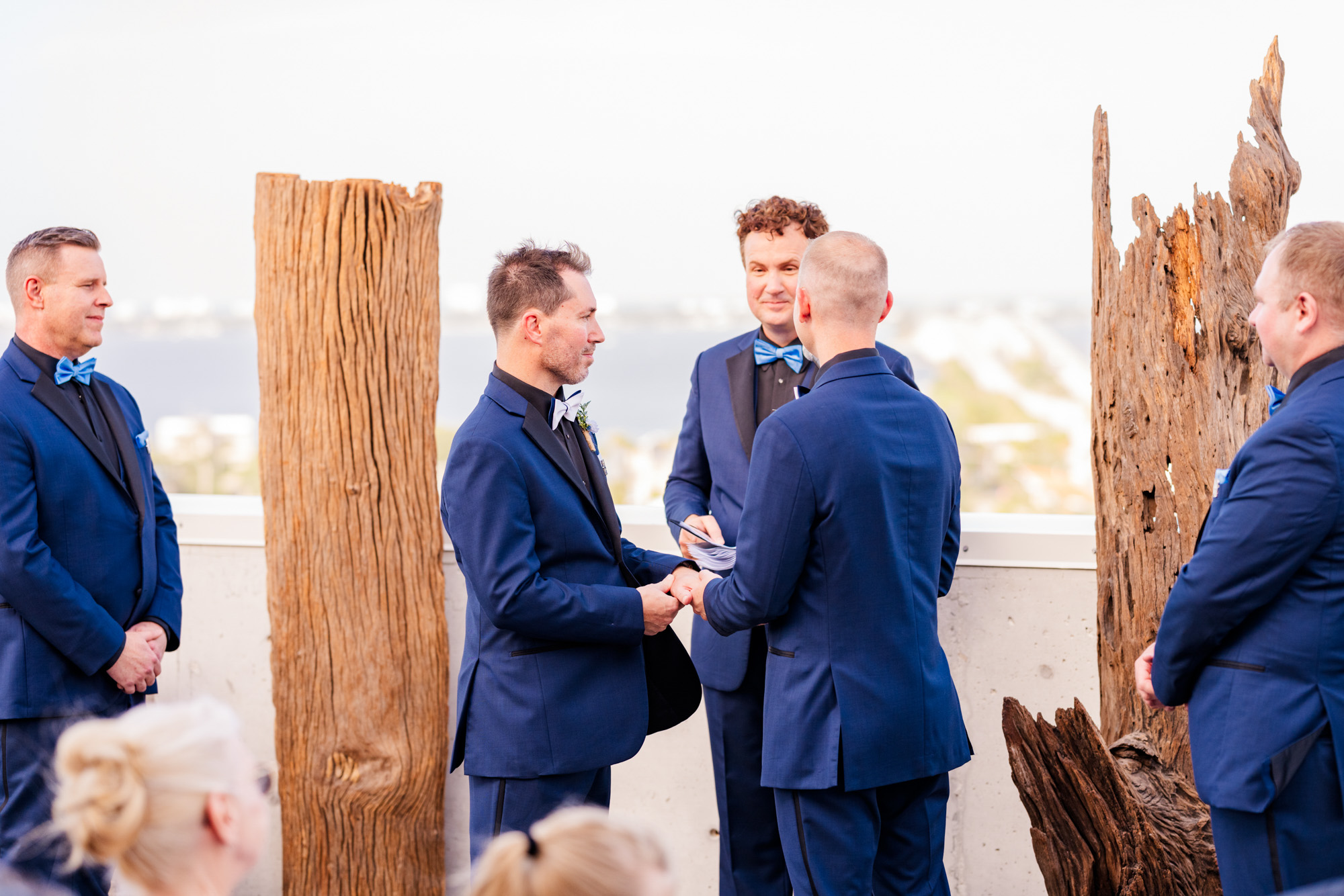 Two grooms holding hands during their wedding ceremony as their officiant stands between them.