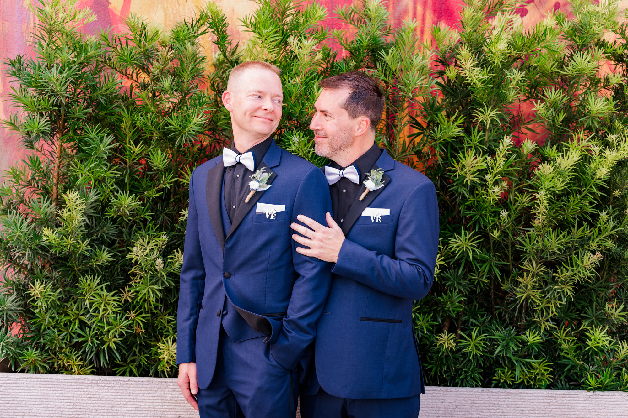 Two grooms looking at each other while posing in matching navy wedding suits.