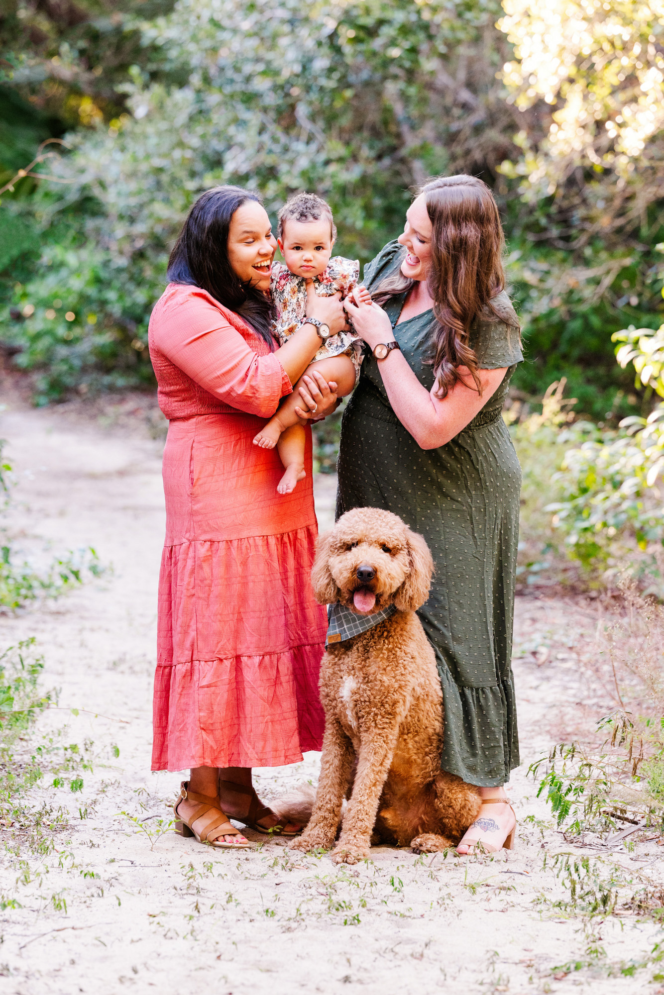 Two mothers smiling at their baby with their curly-haired dog during a Melbourne, Florida family session