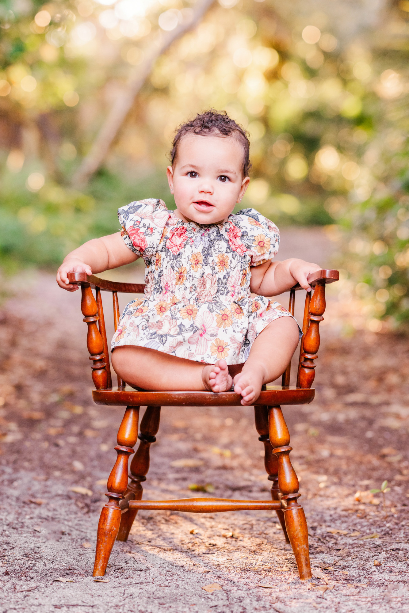 Baby sitting on a small wooden chair surrounded by softly blurred greenery.