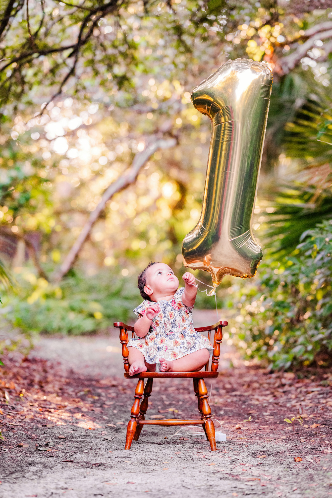 Baby sitting beneath a gold number-one balloon during a first-birthday portrait.