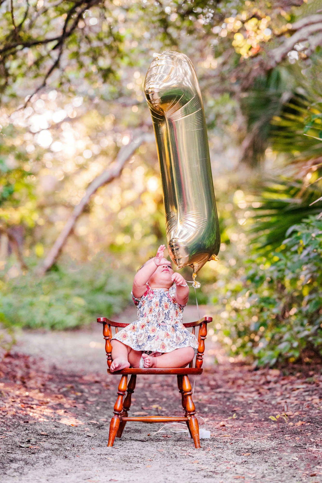 Baby sitting beneath a gold number-one balloon during a first-birthday portrait in Melbourne, Florida