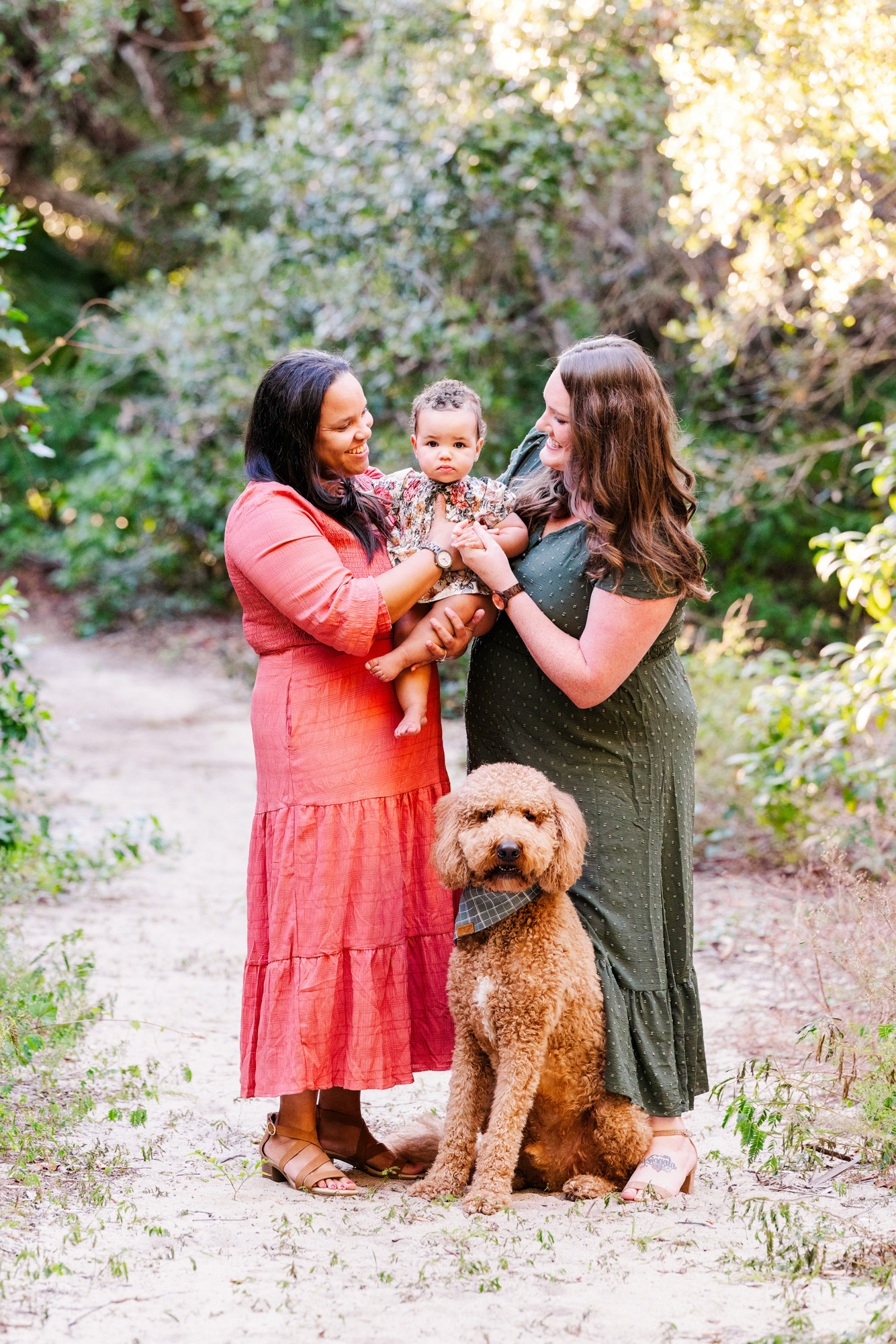 Two moms sharing a playful moment with their baby while their dog sits beside them.