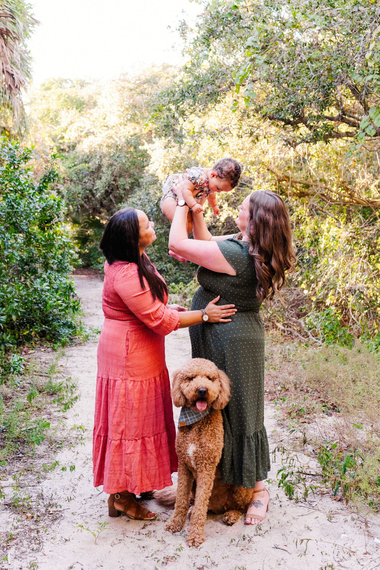 One mother lifting their baby into the air as her partner smiles beside them.