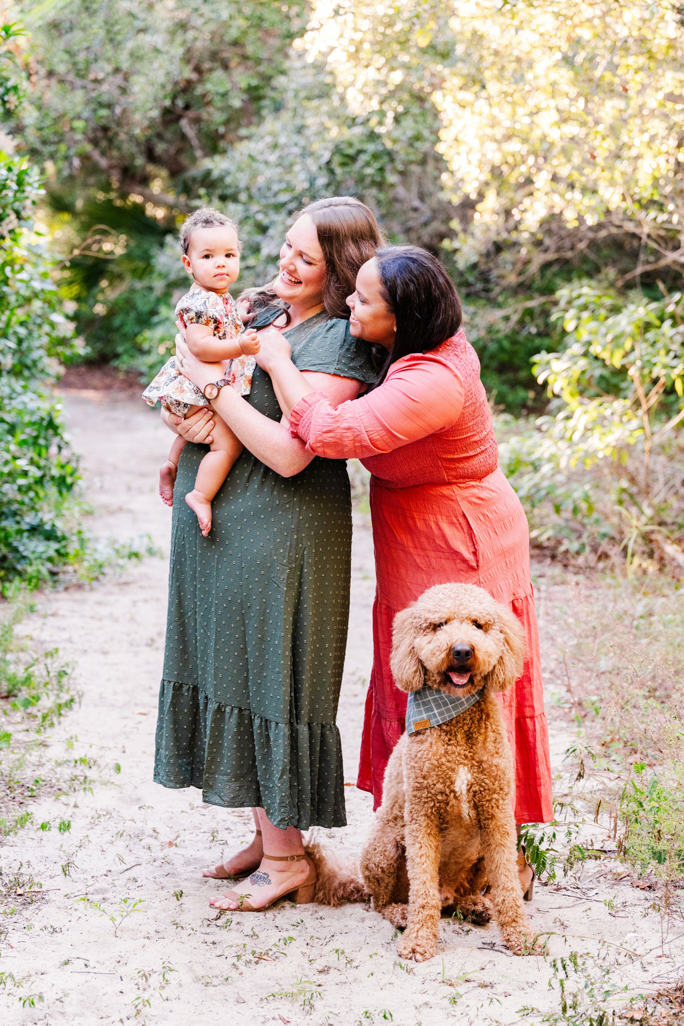 Mother kissing her baby while her partner holds the child and their dog sits nearby.