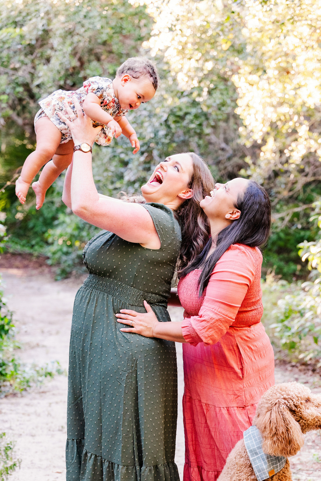 Mother lifting her baby overhead while her partner laughs beside her.