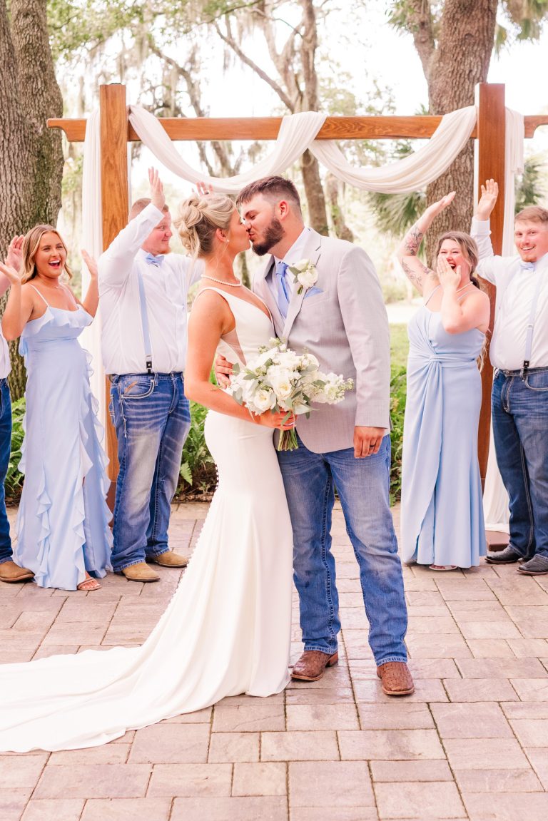 Couple embracing with wedding party cheering behind them during an Up the Creek Farms wedding