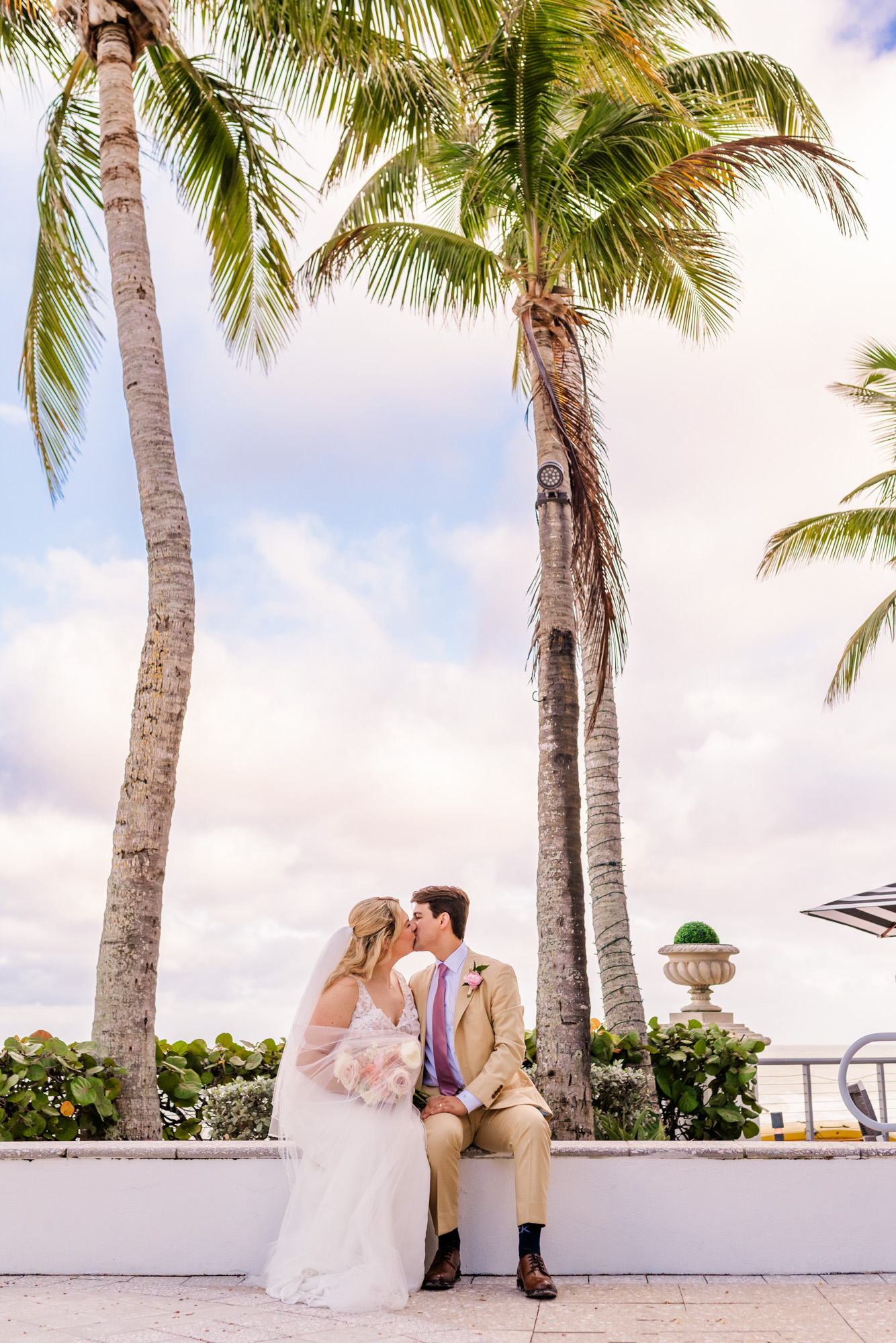 Bride and groom kissing beneath palm trees during their wedding portraits in Vero Beach, Florida.