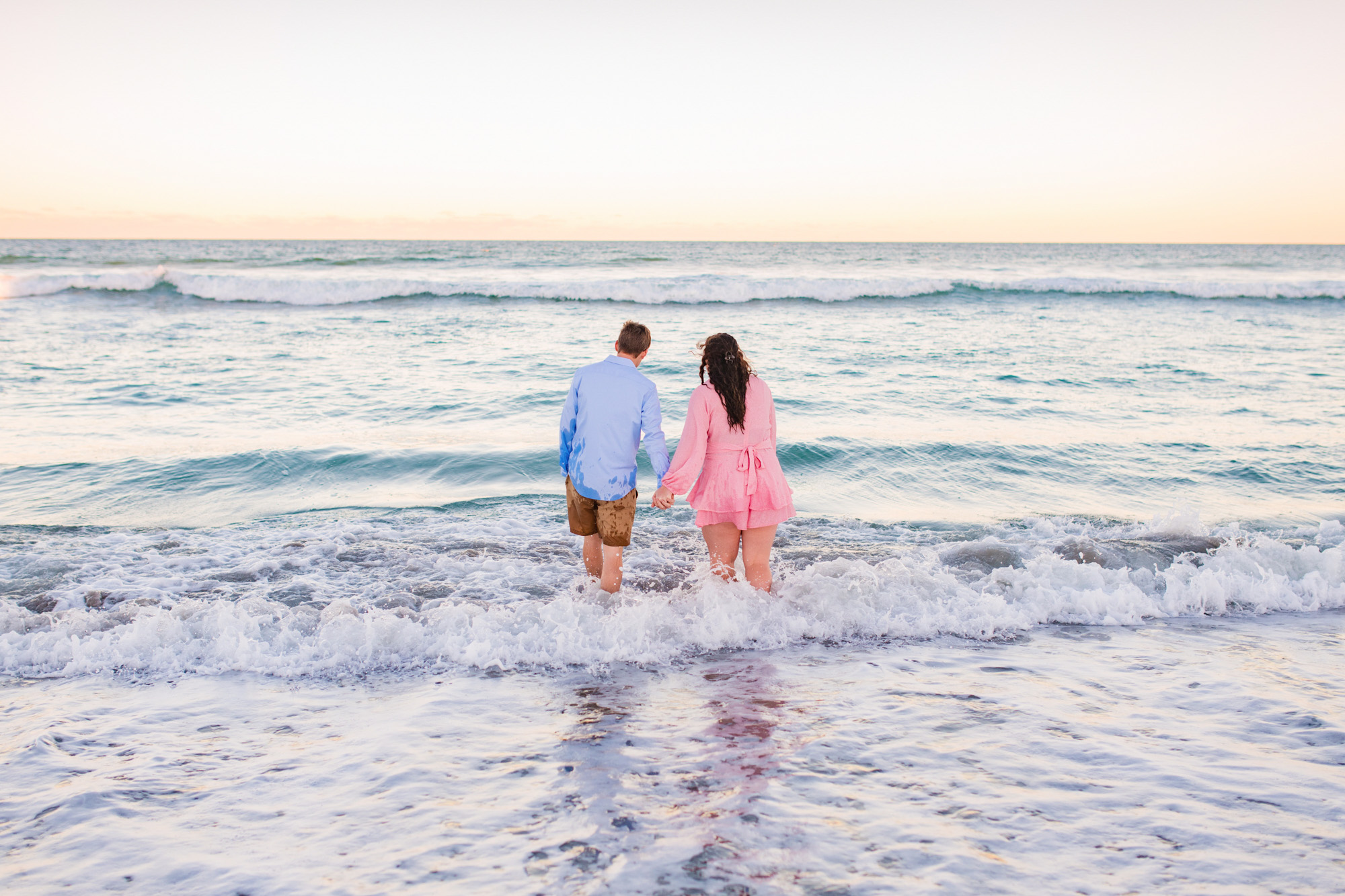 Couple wearing pastels holding hands looking out to the ocean