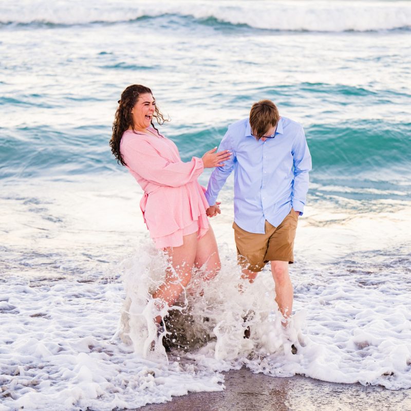Couple in pink and blue laughing at the beach