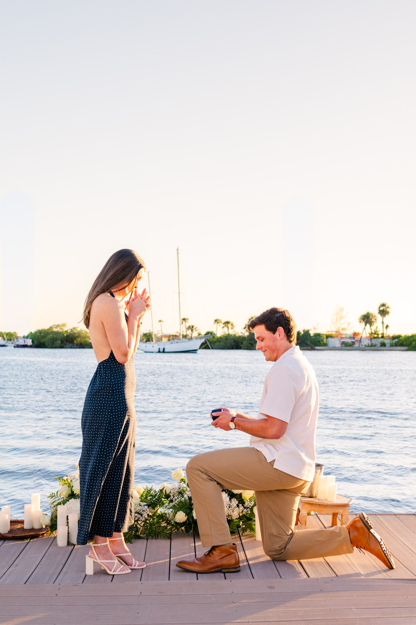 Wide view of a sunset marriage proposal on a dock in Melbourne, Florida, surrounded by white floral arrangements.