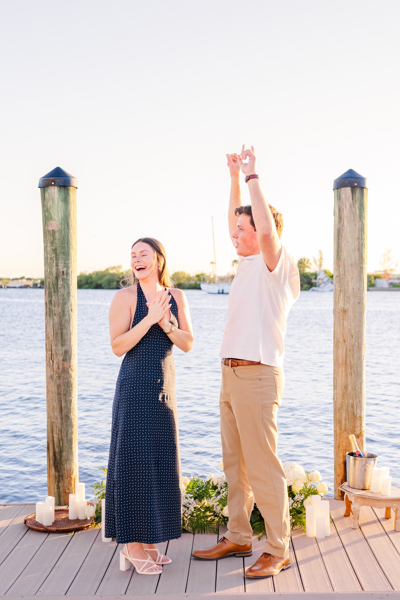 Happy couple celebrates their engagement with raised arms and laughter following a sunset proposal.