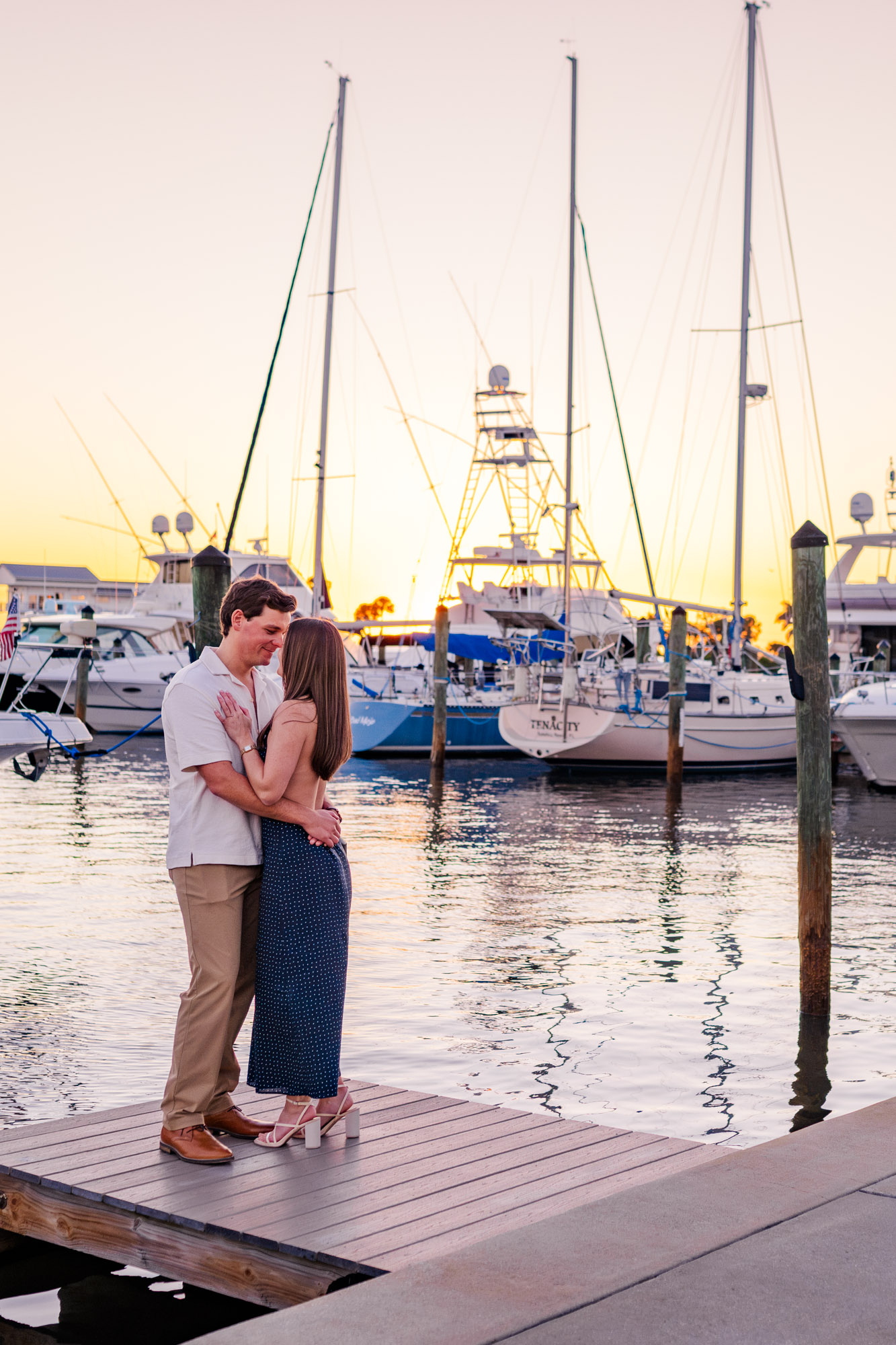 Newly engaged couple embracing on a marina dock surrounded by sailboats during sunset in Melbourne, Florida.