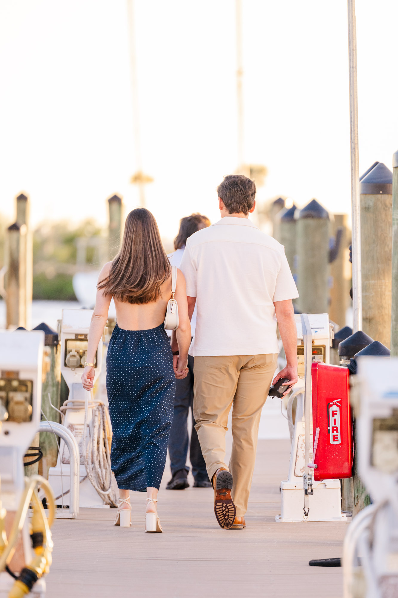 Couple approaching the waterfront proposal location together on a marina dock at golden hour.
