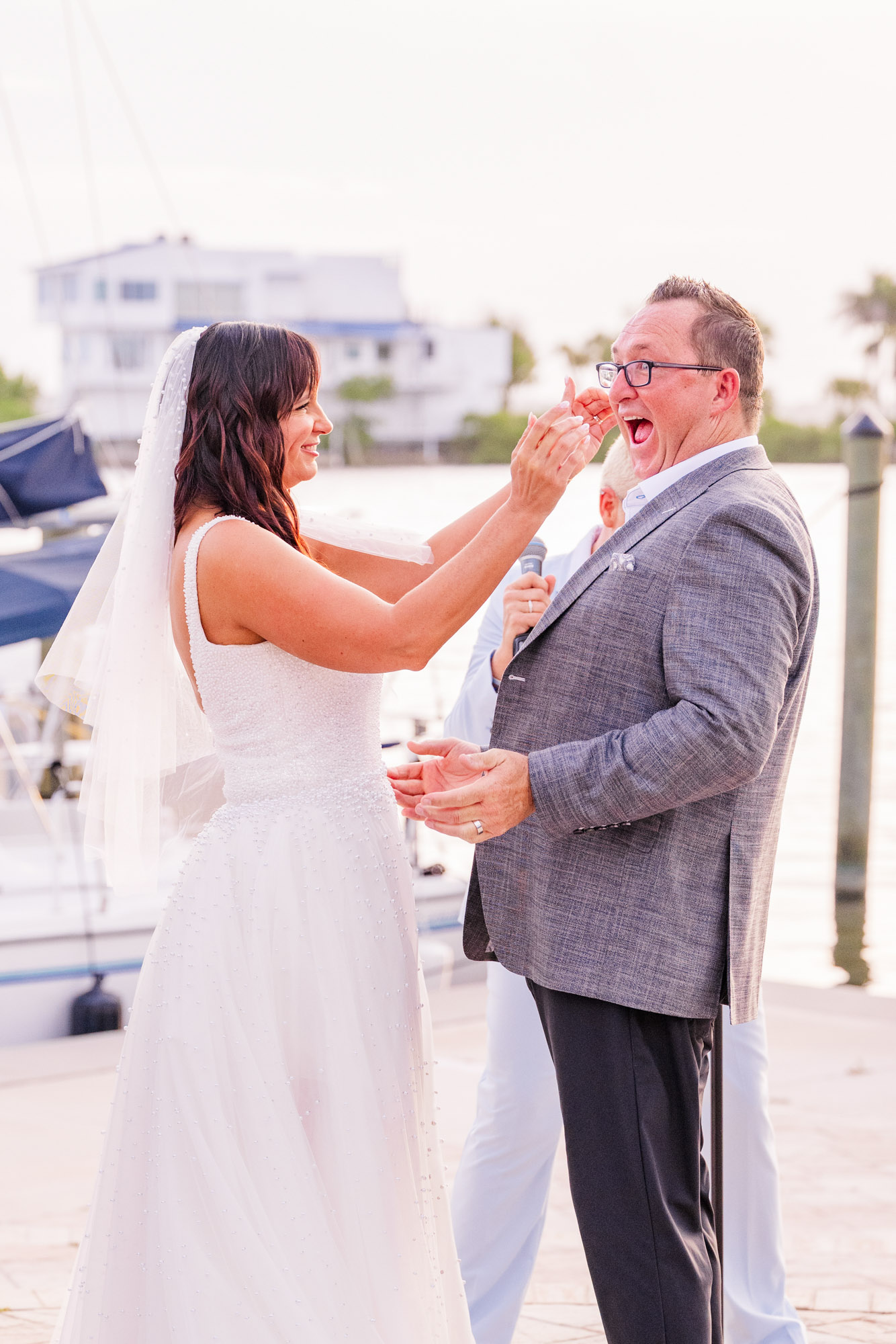 Bride reaching for grooms face while laughing during their wedding ceremony