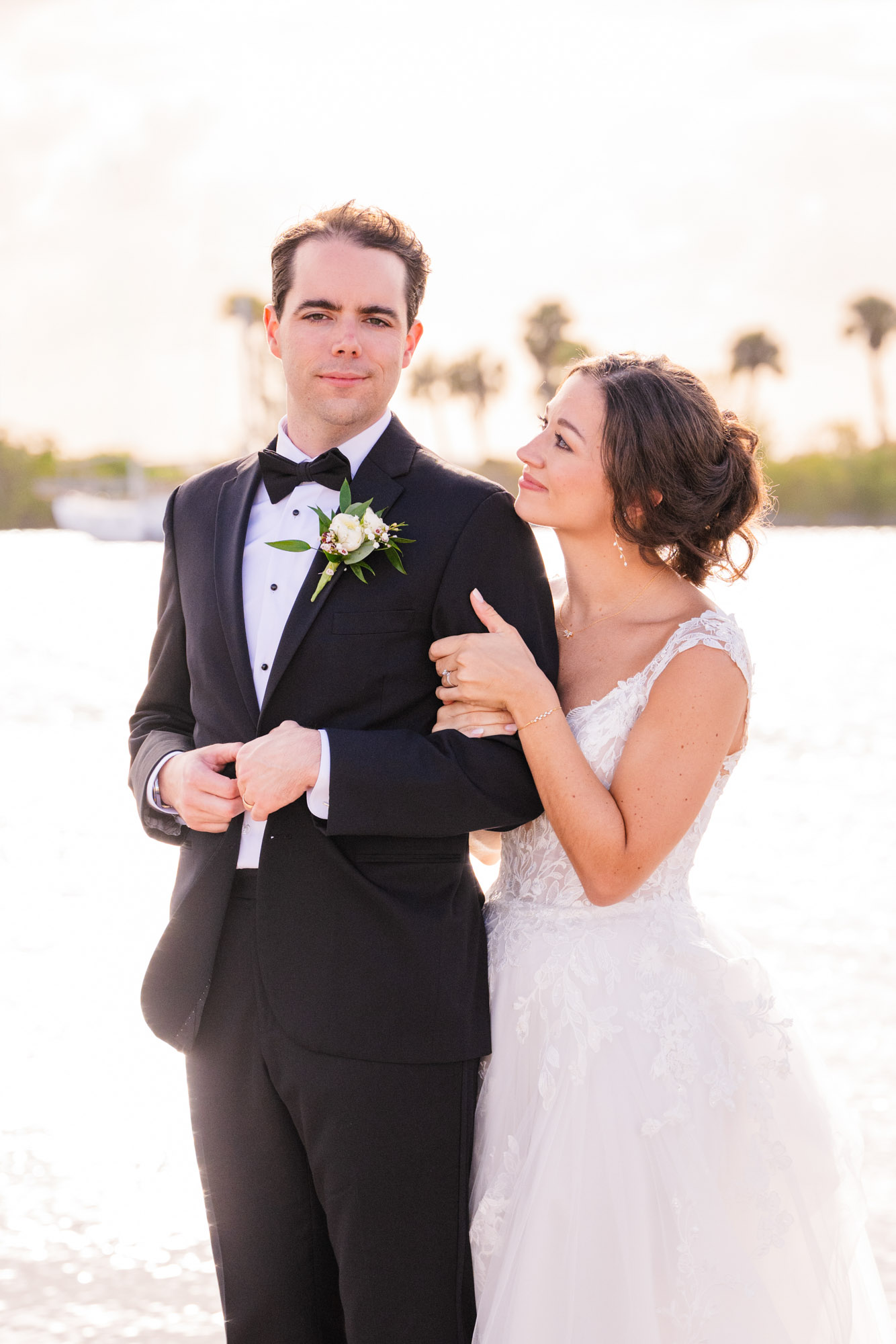Groom in a black tux buttoning a button while bride looks at him