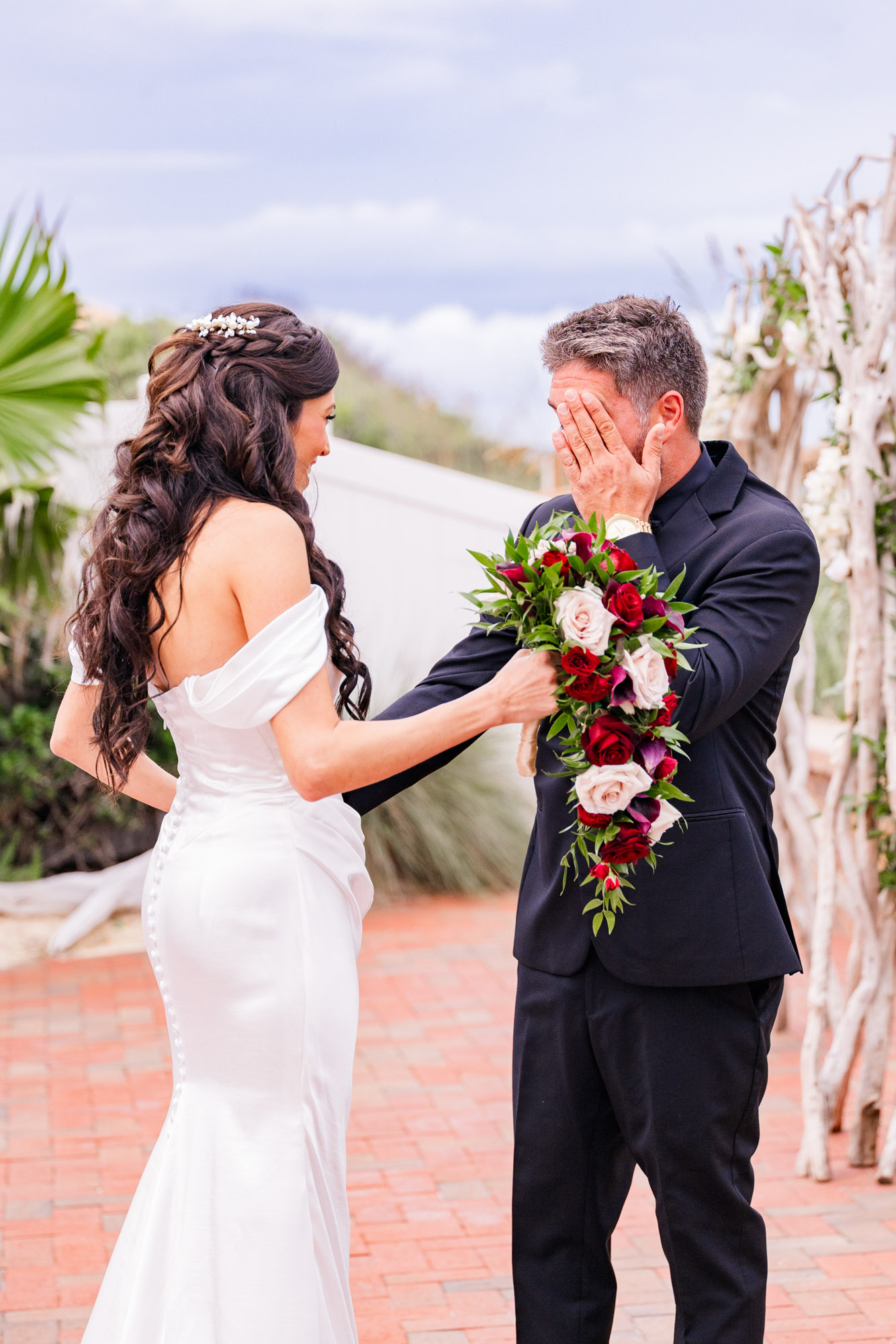 Groom covering his face with his hand as the bride reaches toward him with her bouquet