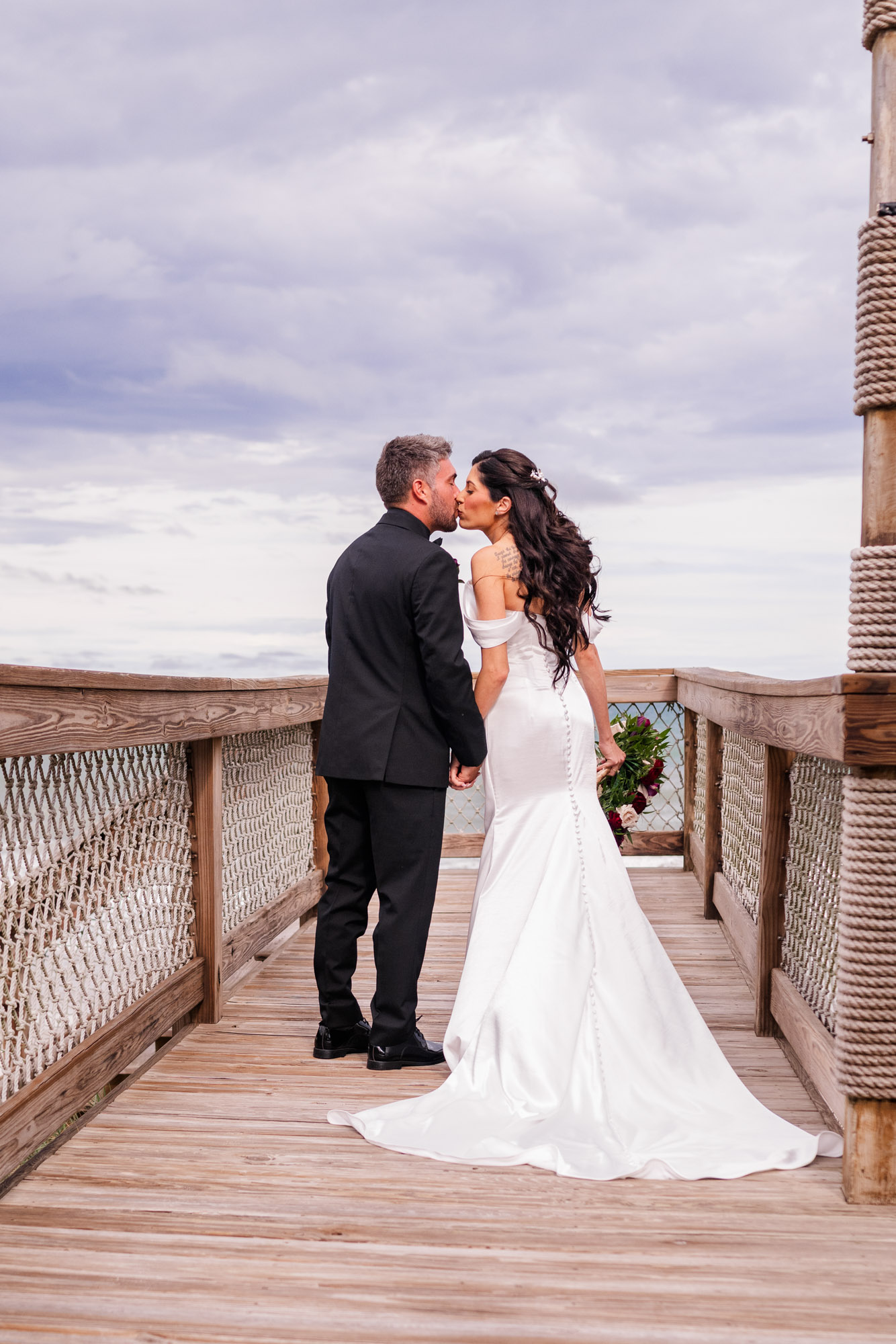 Bride and groom portrait on the brick patio, her train spread out, sea oats and the Atlantic behind