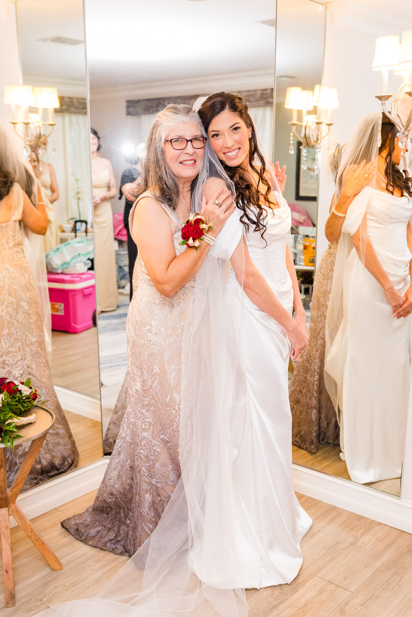 Bride and her mother cheek to cheek in the bridal suite, both smiling, veil over the bride’s shoulder