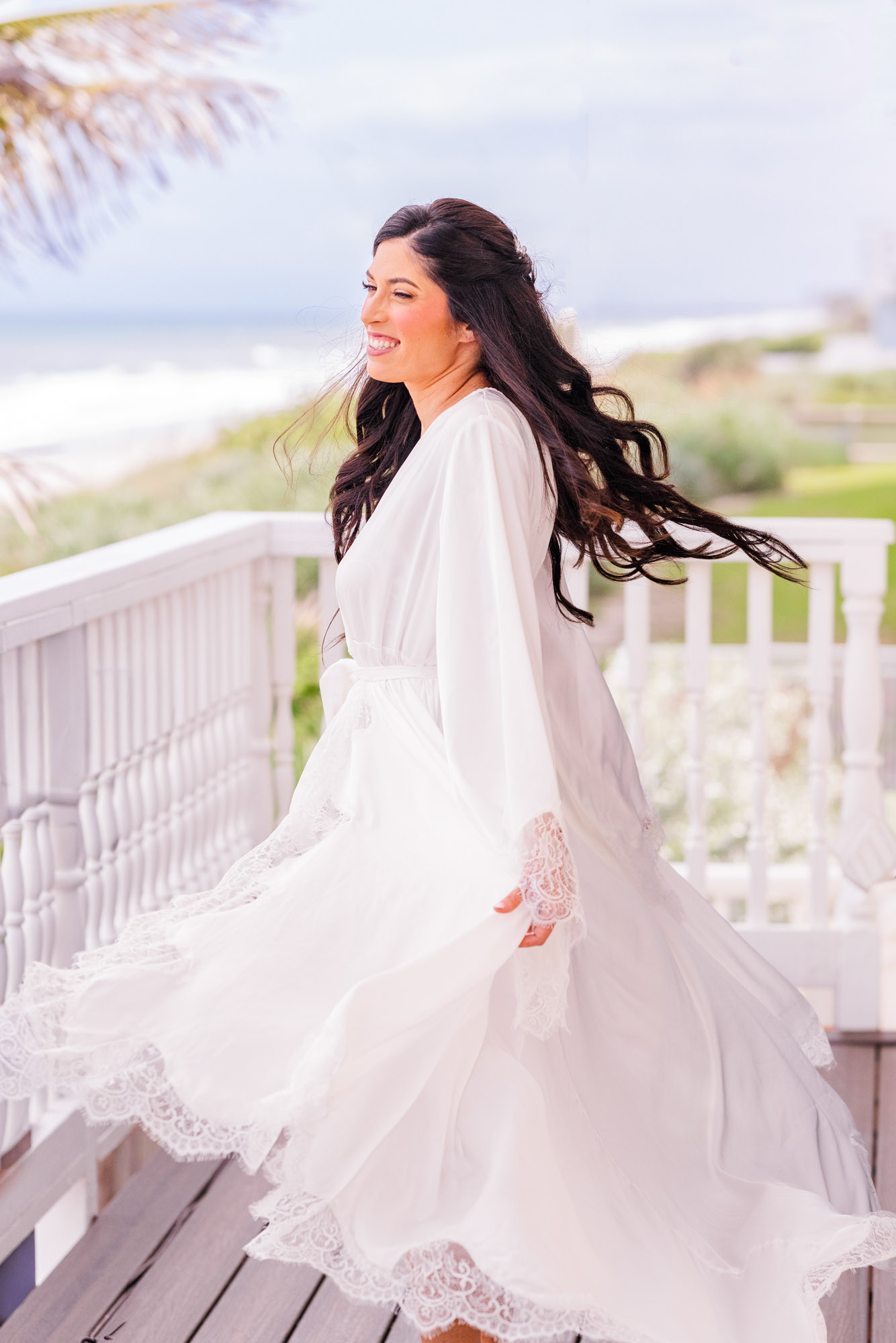Bride spinning in a white lace robe, hair and fabric caught mid-air beneath a palm