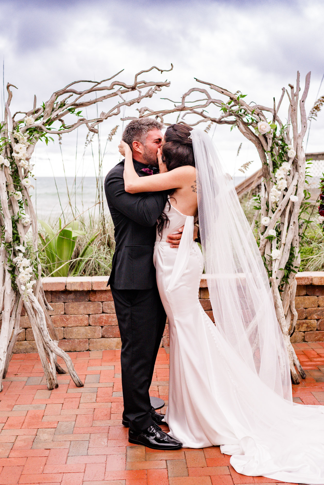 Bride and groom’s first kiss as a married couple beneath the driftwood arch