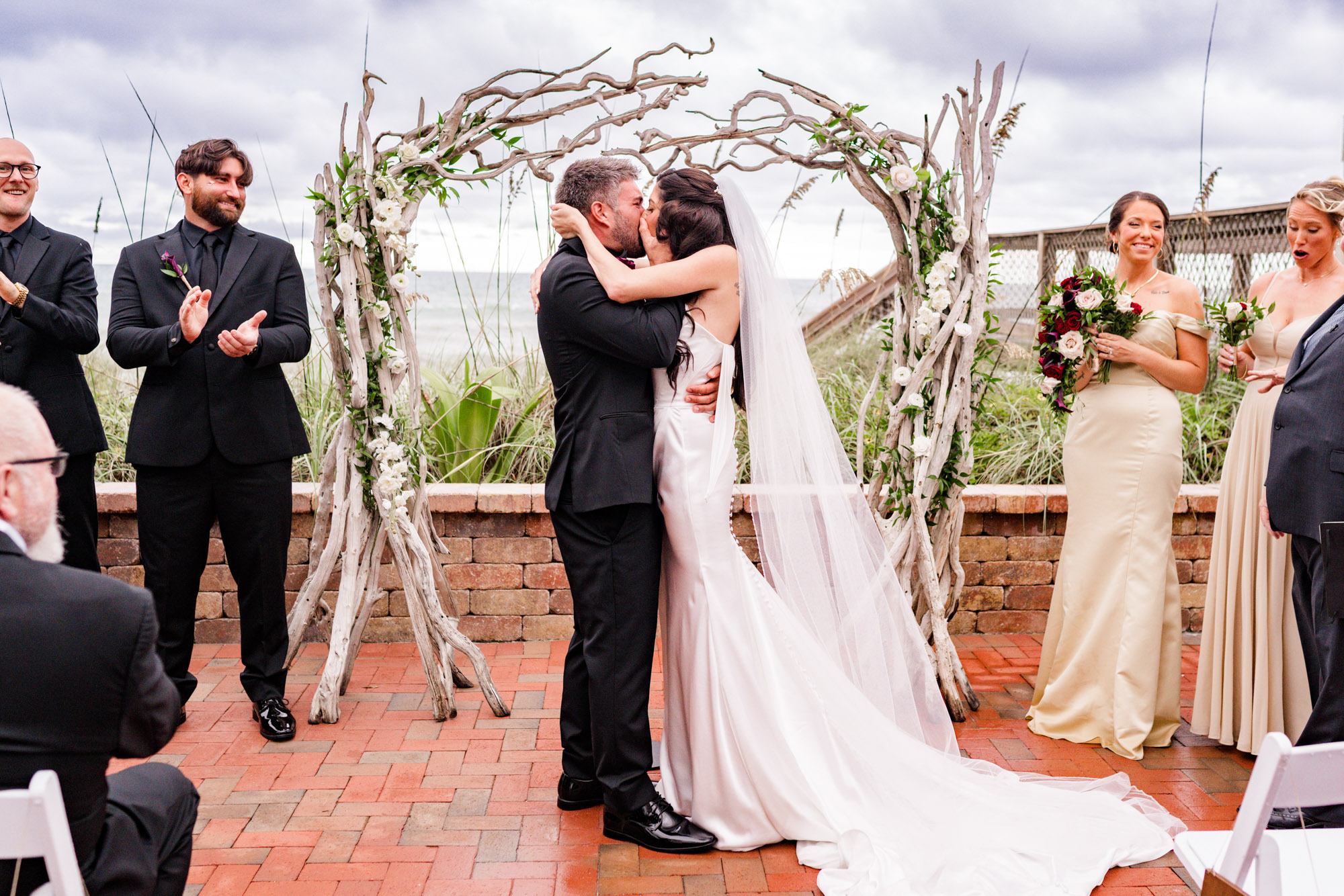 The first kiss, groomsmen applauding and bridesmaids looking on