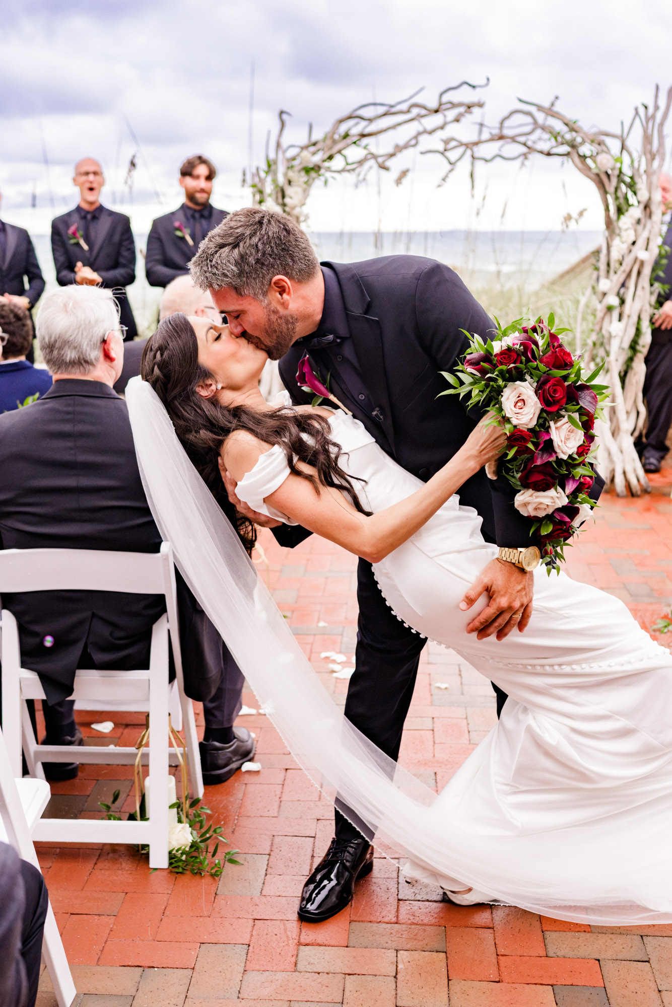 The dip kiss in the aisle, her cascading bouquet of red roses and calla lilies held out beside them