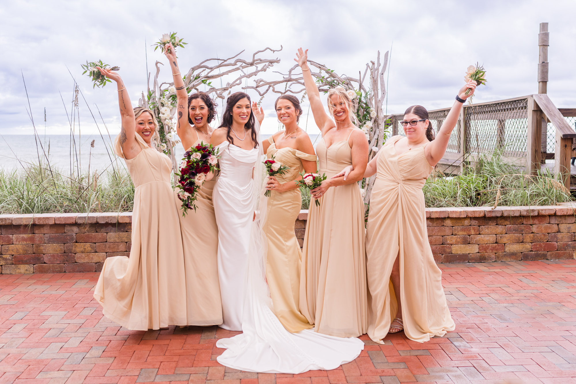 Bridesmaids cheering with their bouquets raised, the bride laughing in the middle