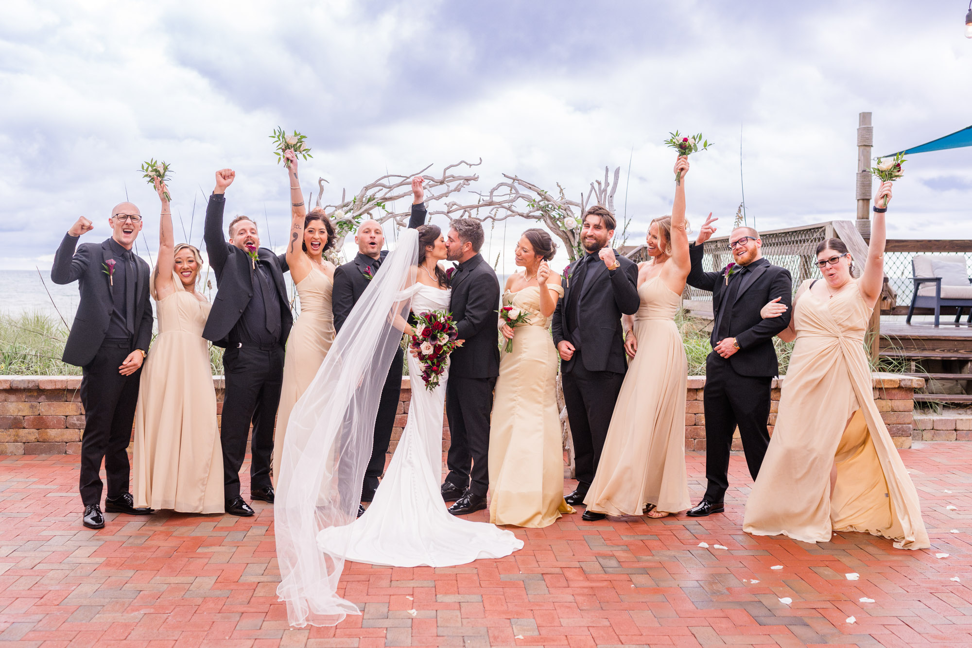 Wedding party cheering with arms raised as the bride and groom kiss in the middle