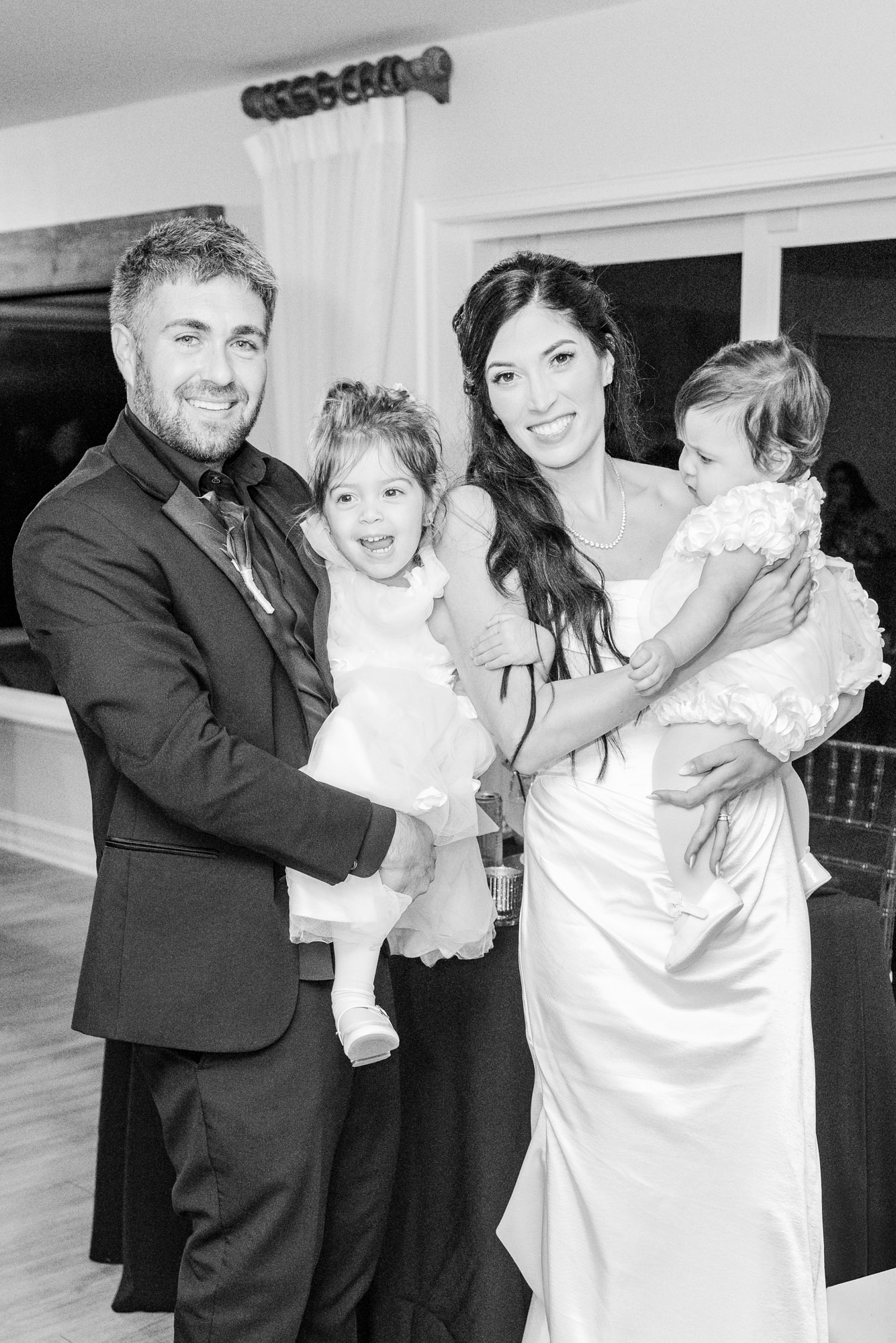 Black and white portrait of the newlyweds each holding one of the children at the reception