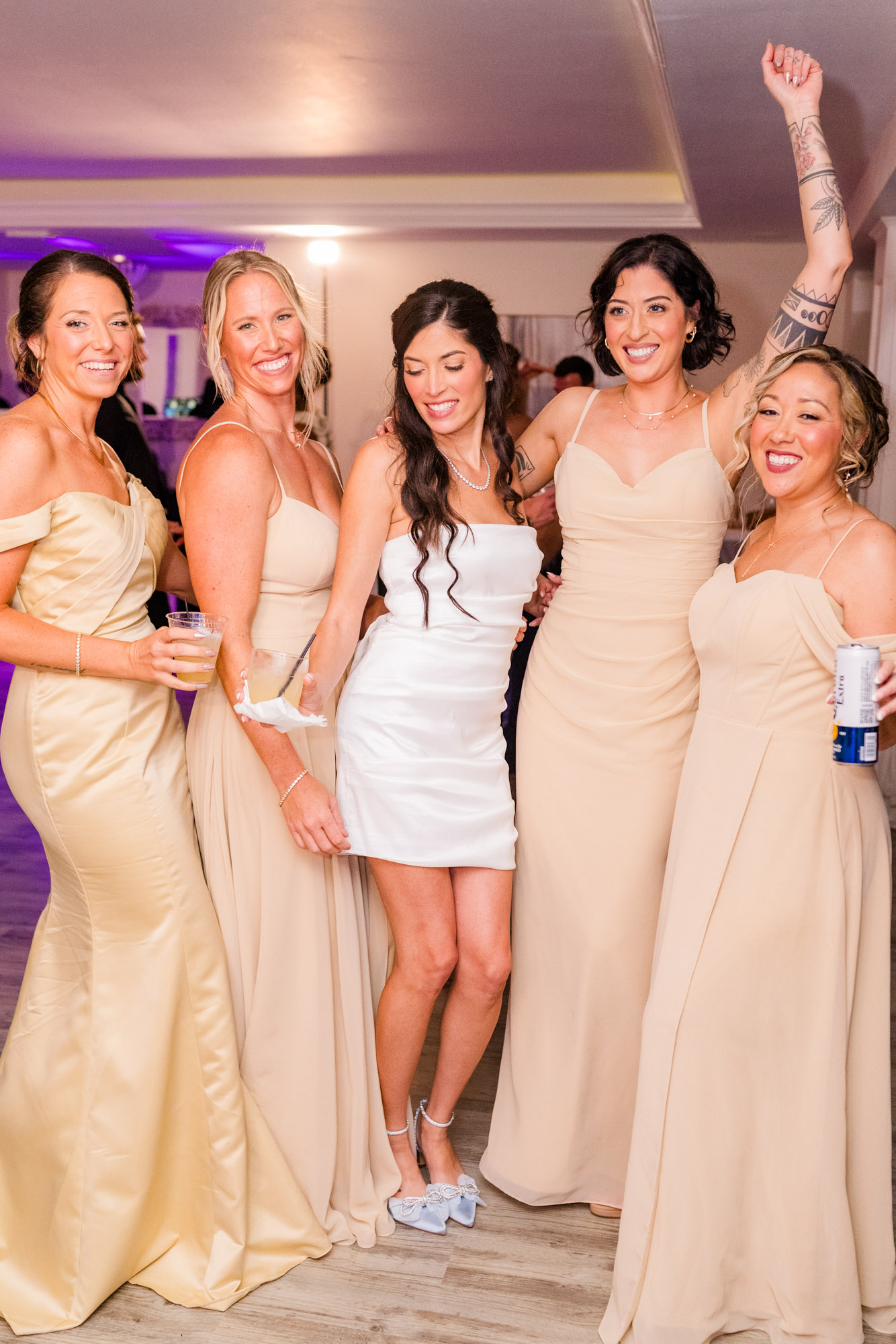 Bride and her bridesmaids laughing on the dance floor, one with her arm thrown in the air