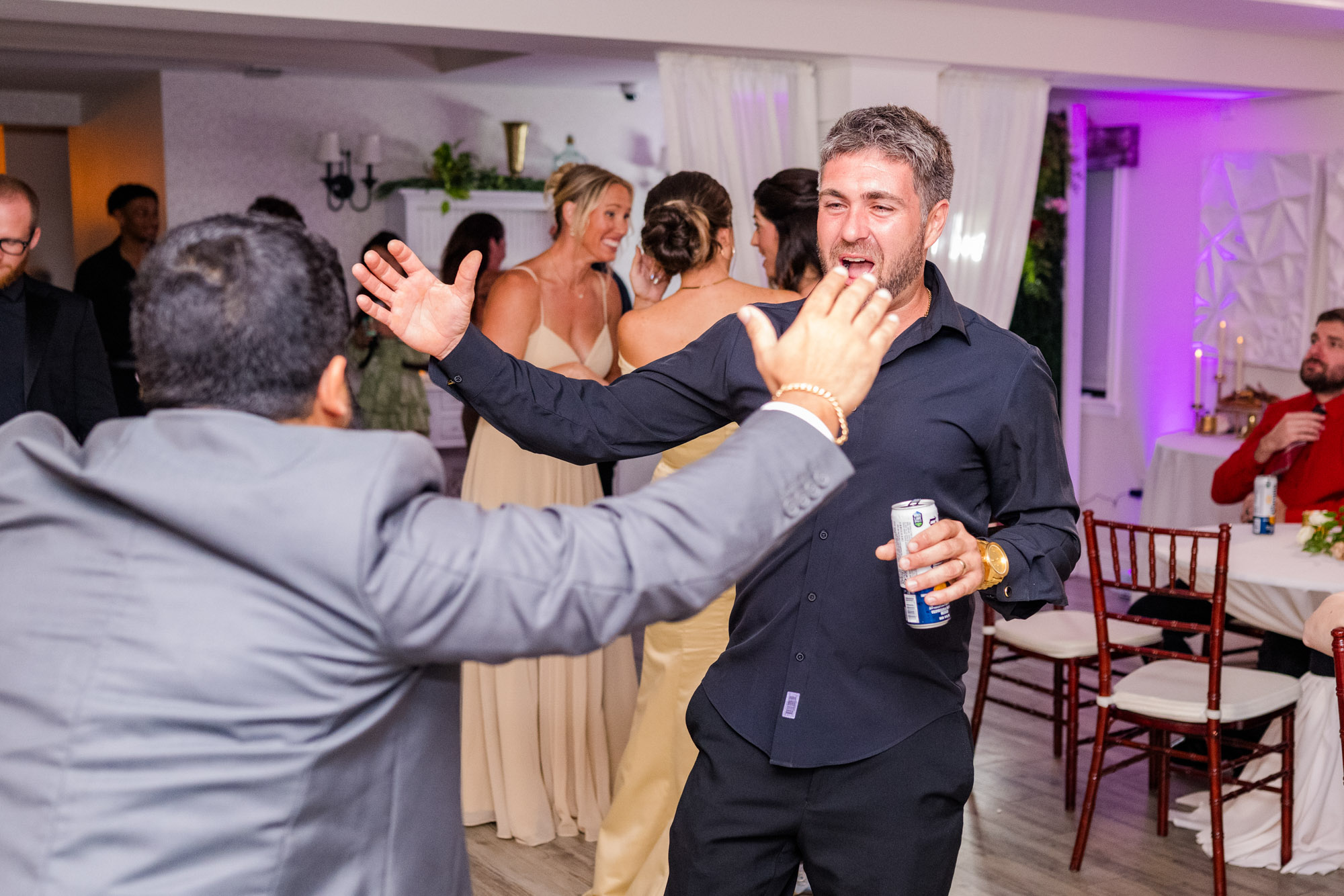 Groom with his arms thrown wide on the dance floor, mid-laugh