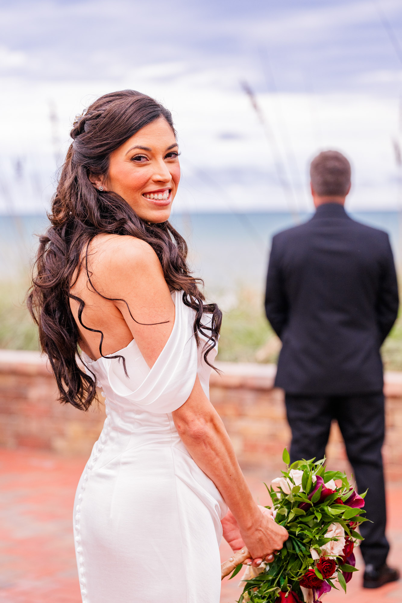 Bride looks back over her shoulder on the beach boardwalk, her train spread down the steps behind her