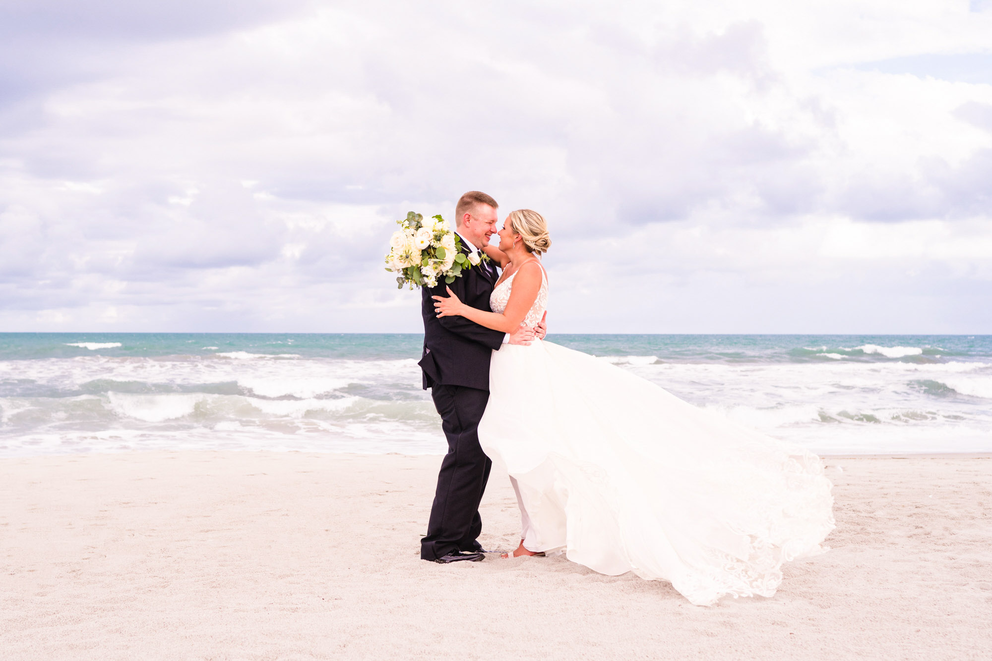 Bride and groom kissing on the beach with the brides dress blowing in the wind on Melbourne Beach