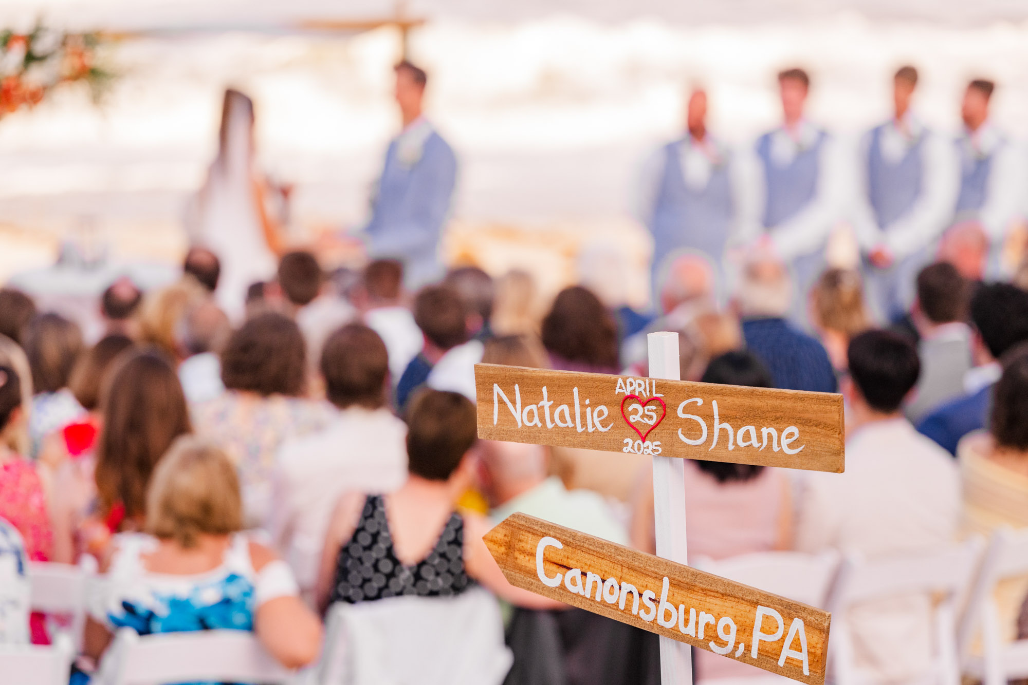 sign stating couples names with blurred out view of the ceremony in the background