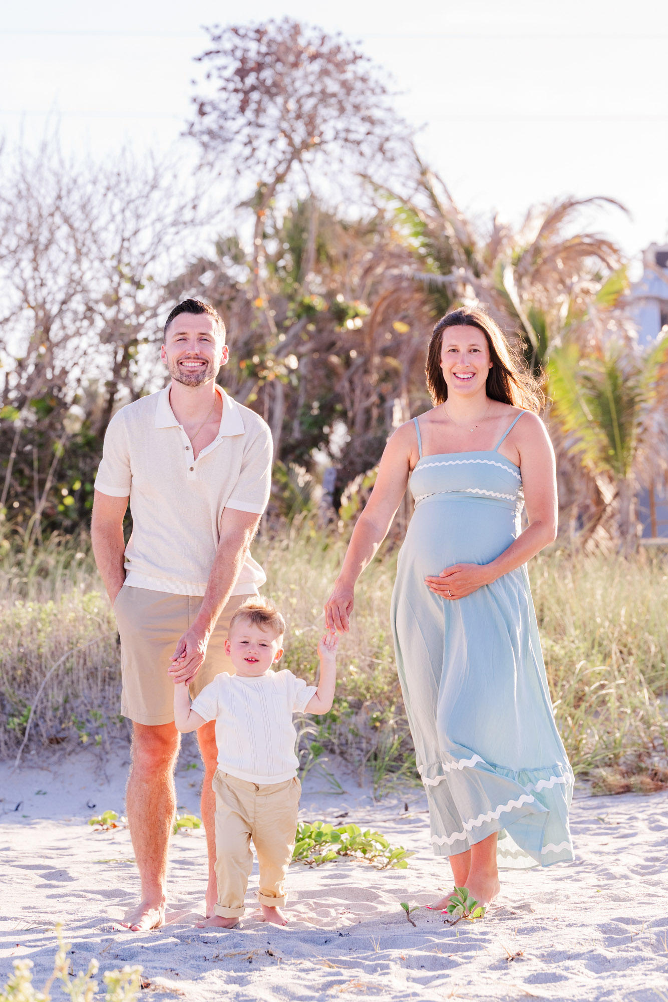 Parents walking hand in hand with their toddler during a beach maternity and family session.