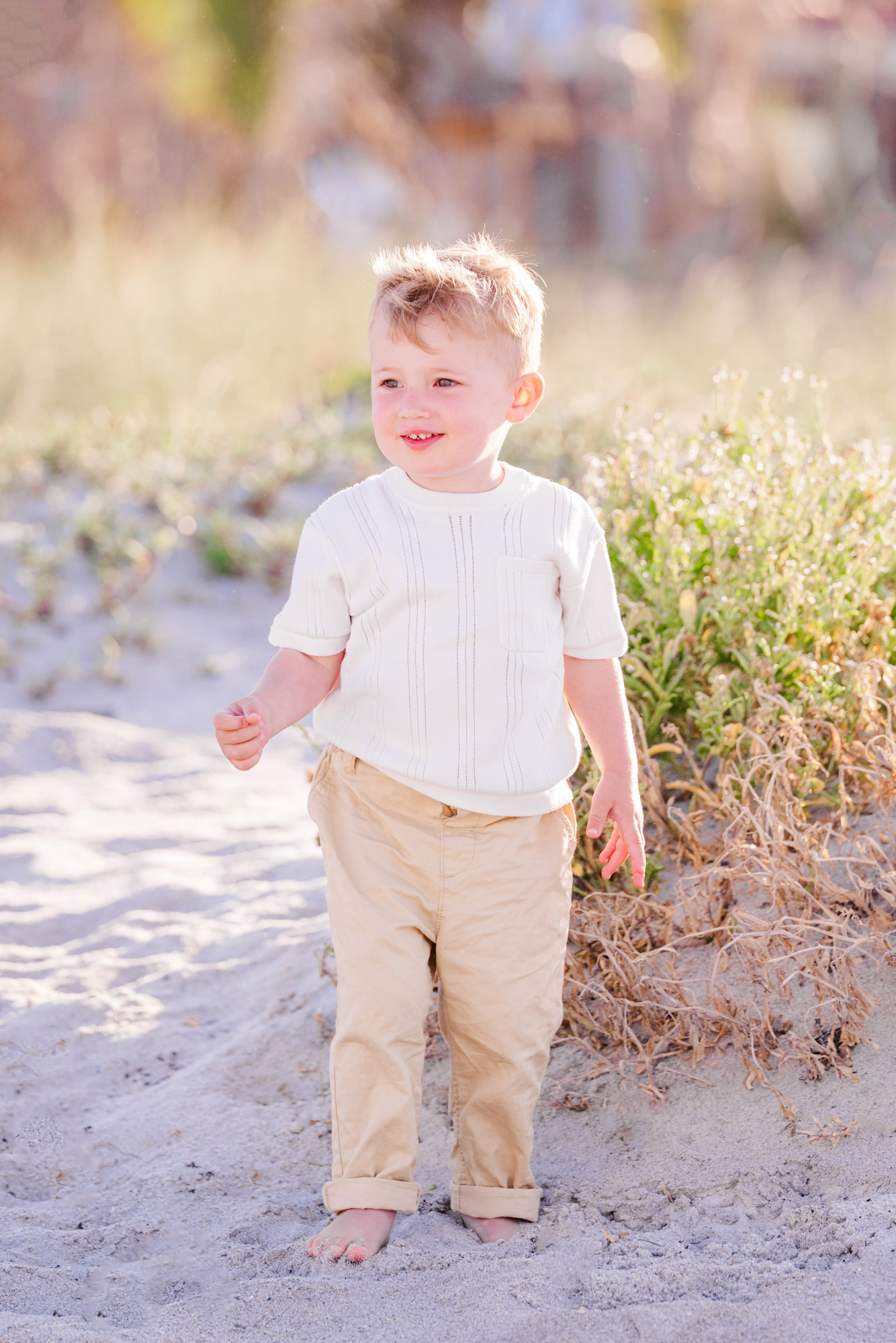 Young boy standing barefoot in the sand during a family beach photo session.