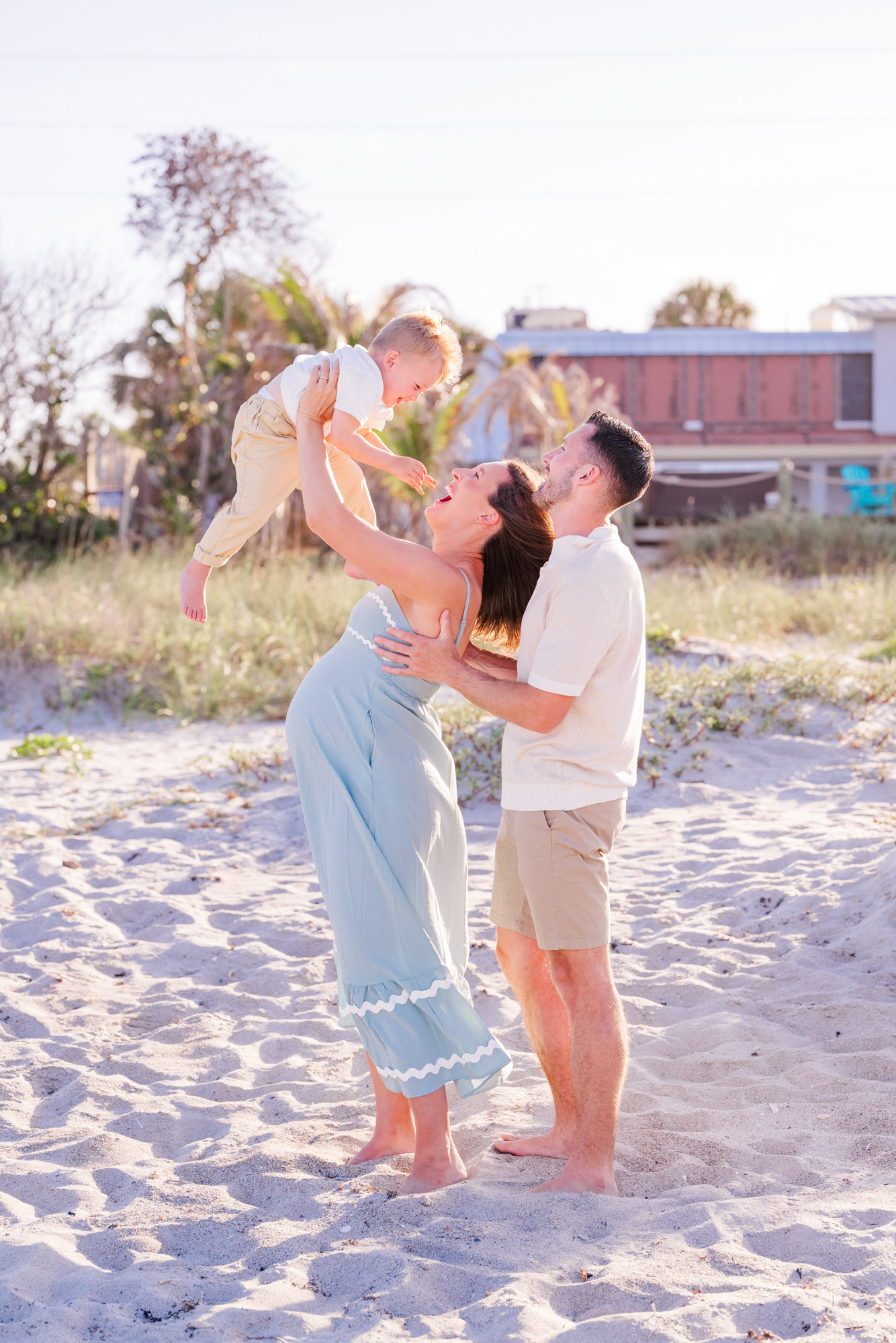 Parents lifting their young son into the air during a playful beach family session.