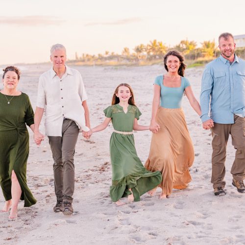 Multigenerational family walking hand in hand along the beach at golden hour.