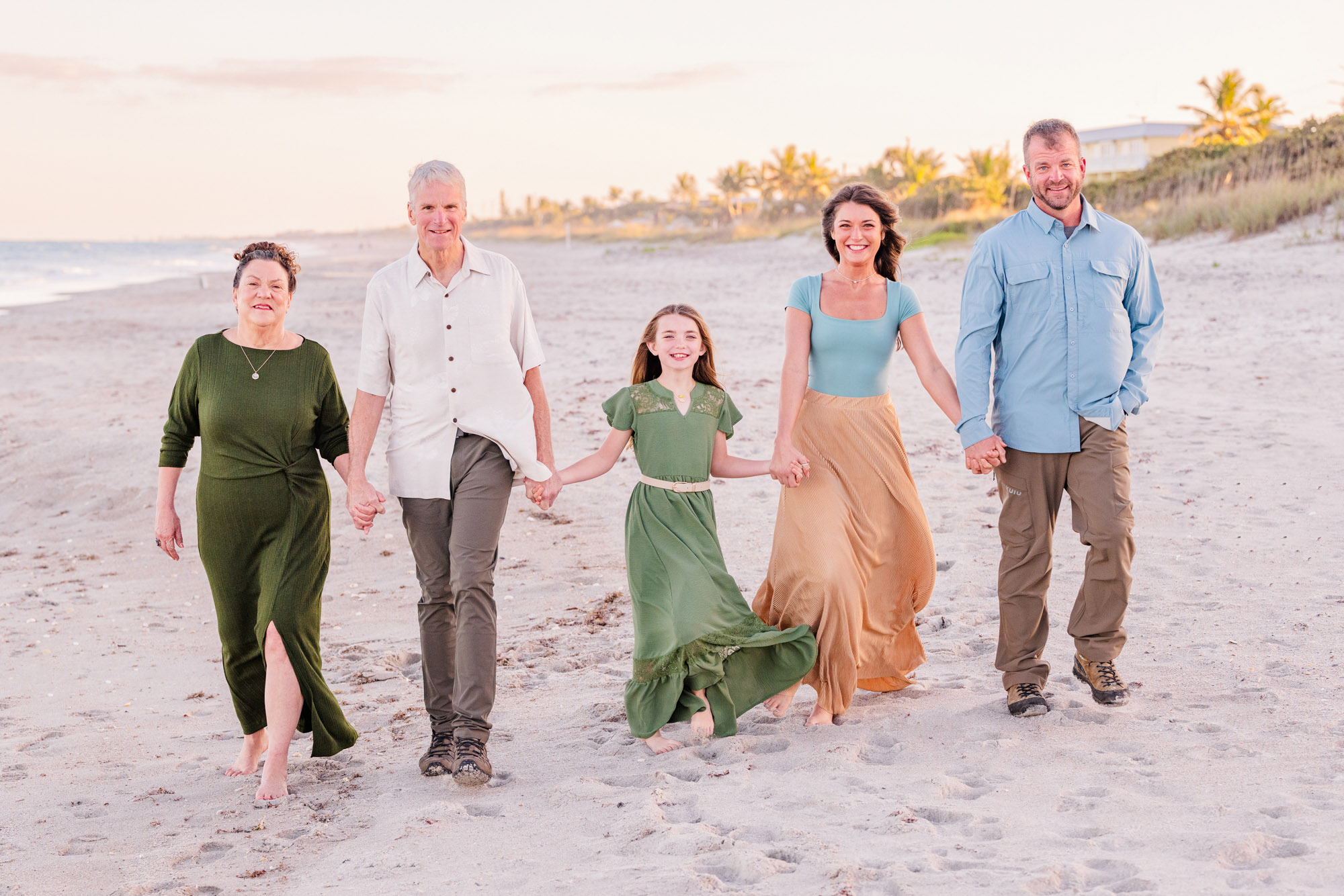 Multigenerational family walking hand in hand along the beach at golden hour.