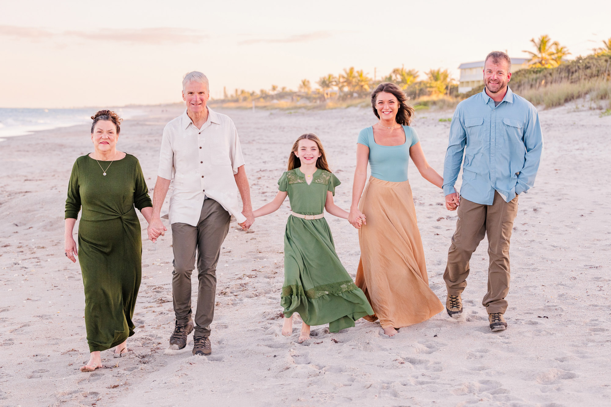 Family walking barefoot together on the sand during a sunset beach photo session.