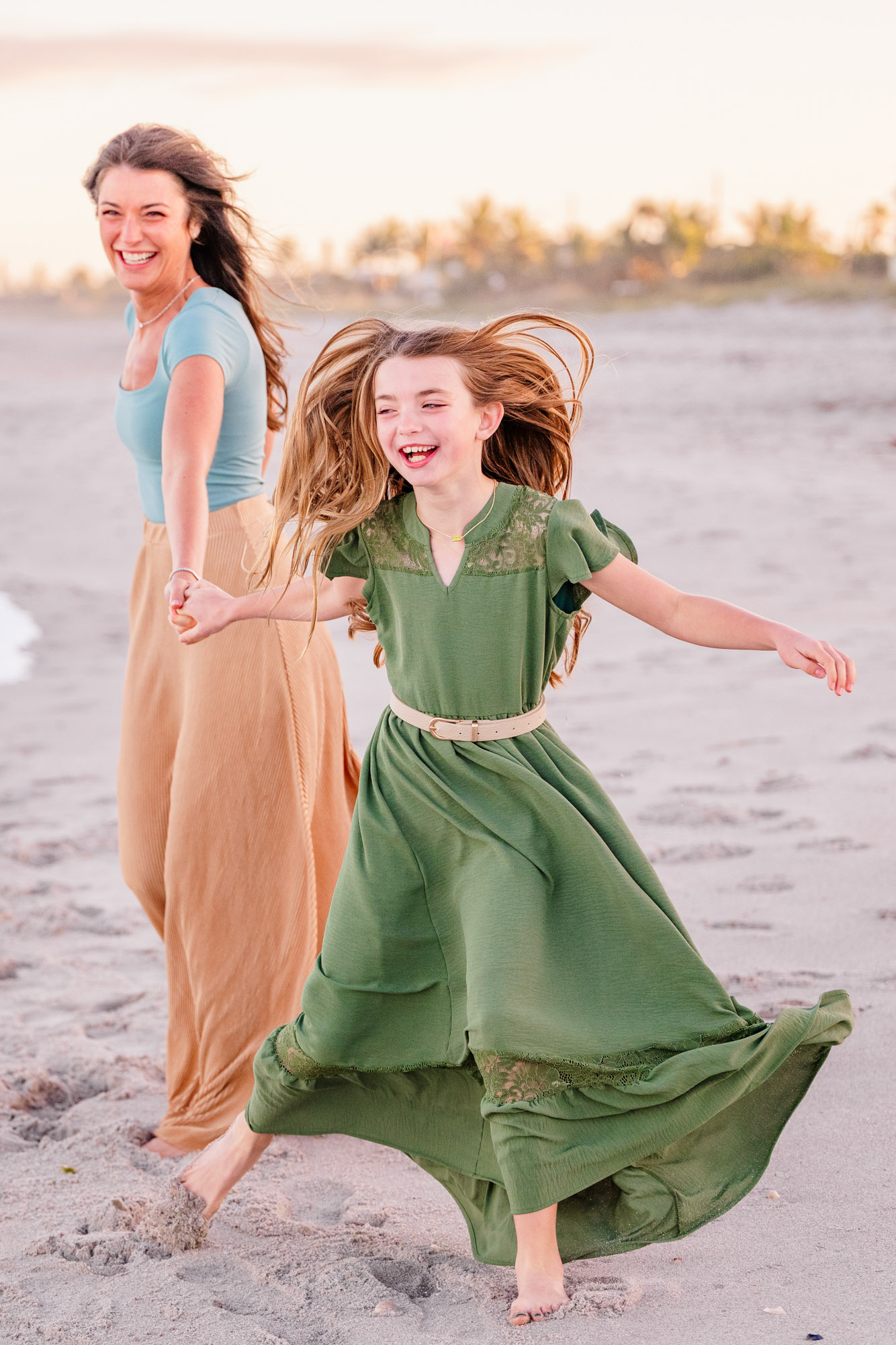 Mother and daughter laughing and running together on the beach in the evening light.