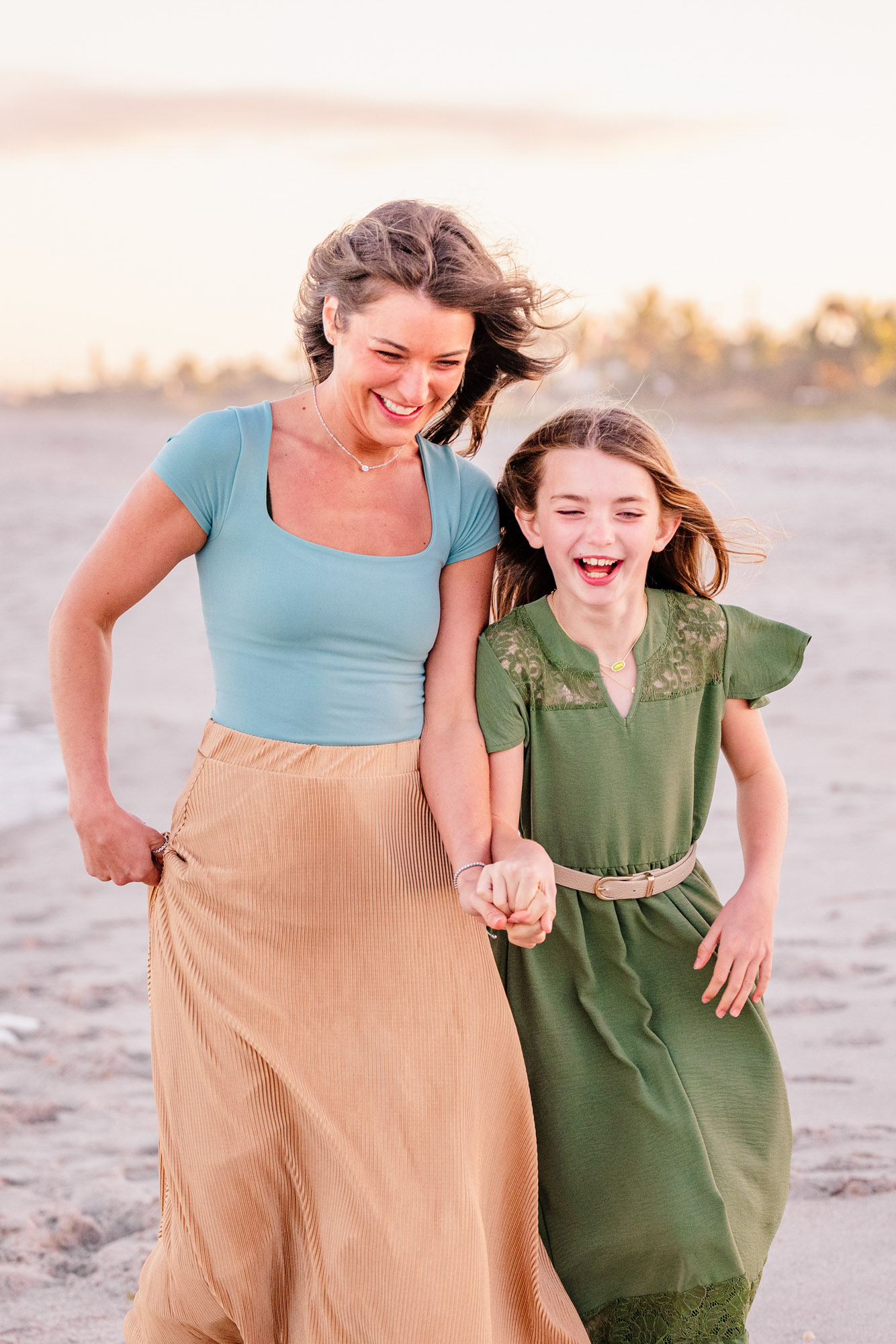 Mother and daughter smiling and holding hands during a relaxed family beach session.