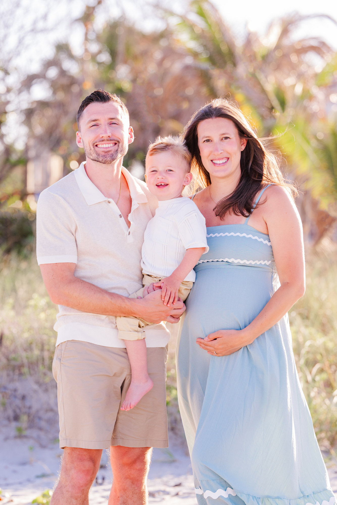 Expecting parents with their young son posing together on the beach in Melbourne Beach