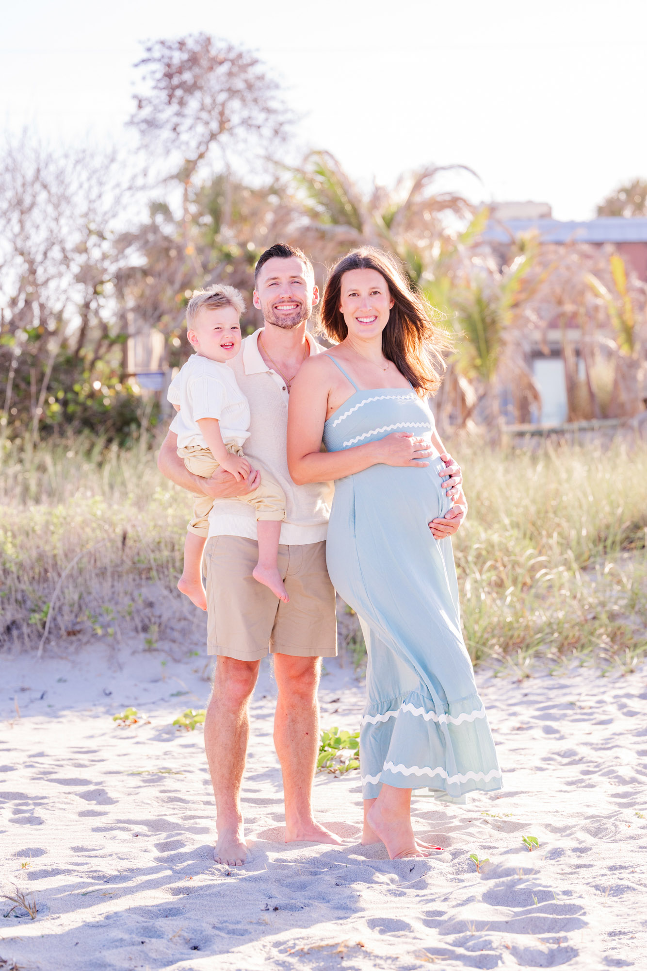 Pregnant mother, father and young son smiling together during a beach family session.