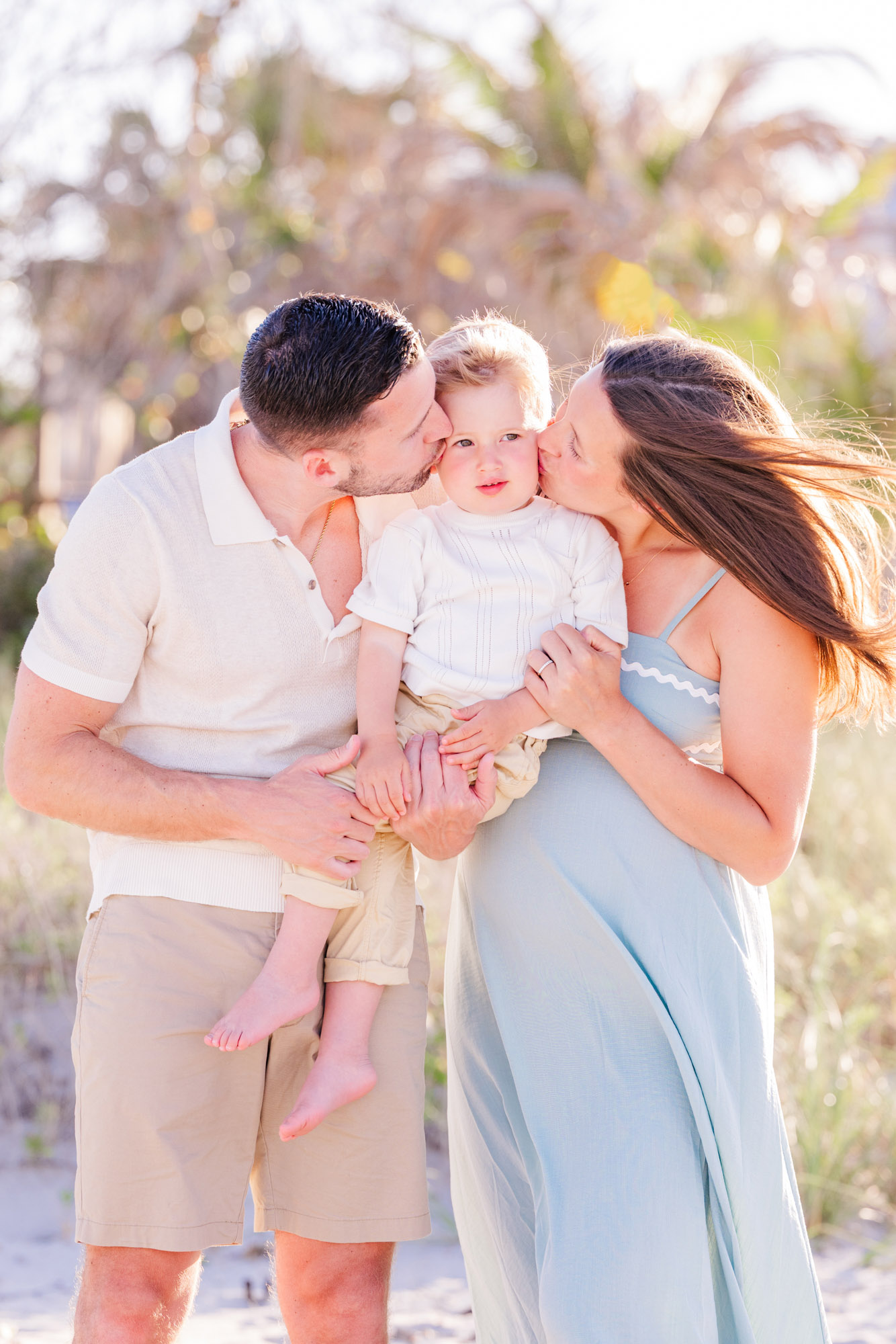 Parents kissing their young son during a candid family photo on the beach.